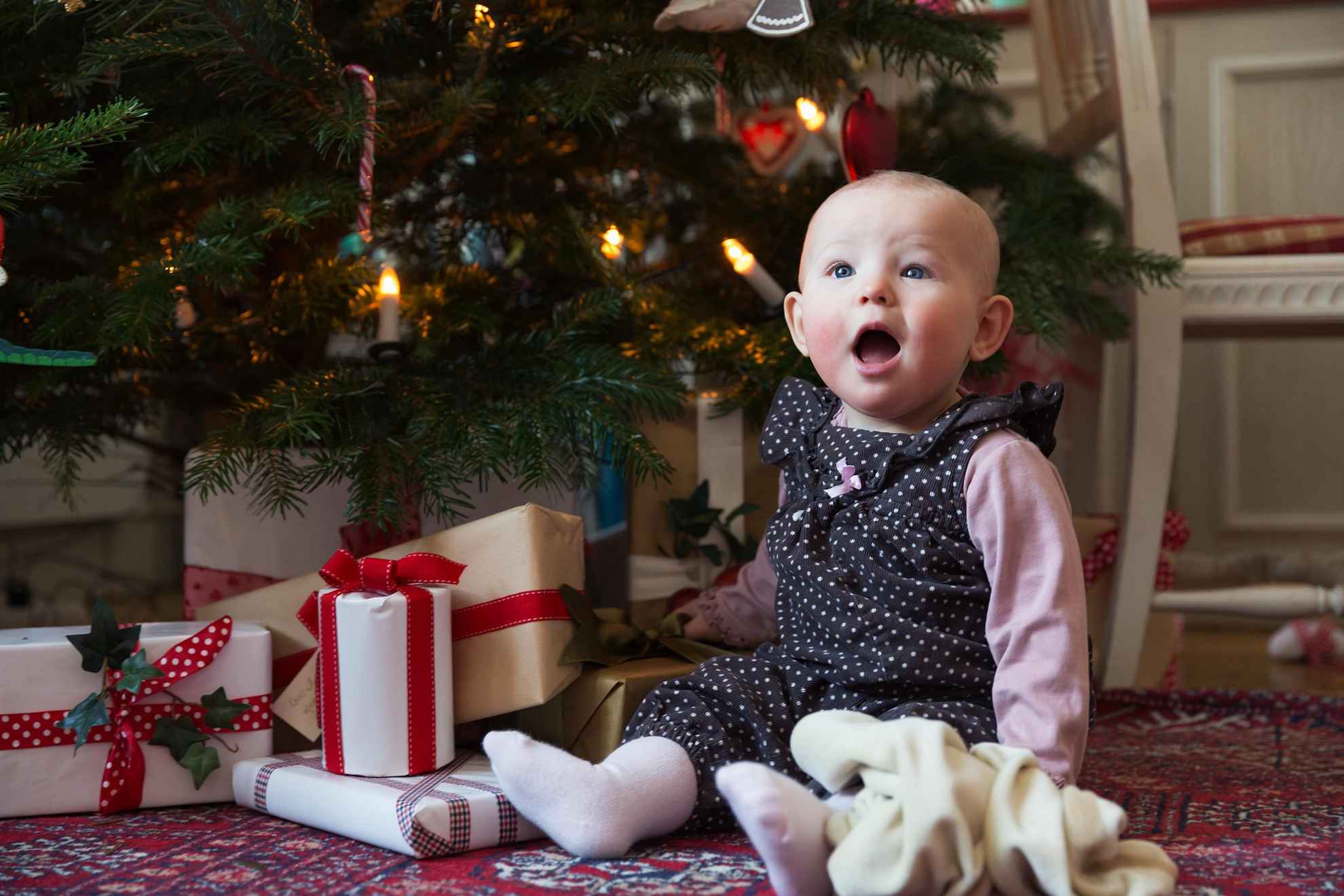 Een baby zit naast de pakjes die onder de kerstboom liggen.