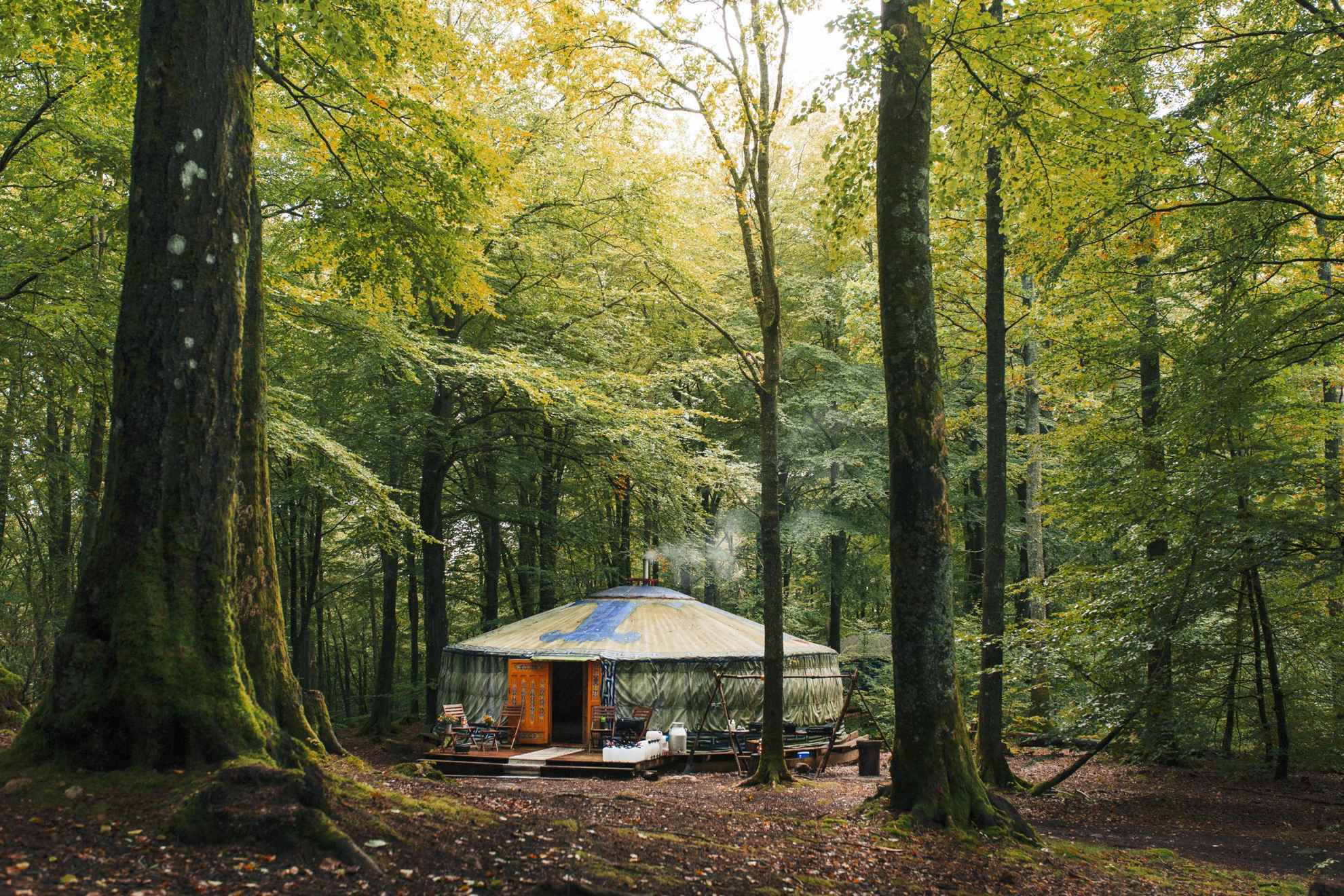 Rook komt uit de schoorsteen van het ronde Nyrups Naturhotell omgeven door weelderige bosvegetatie en bomen.