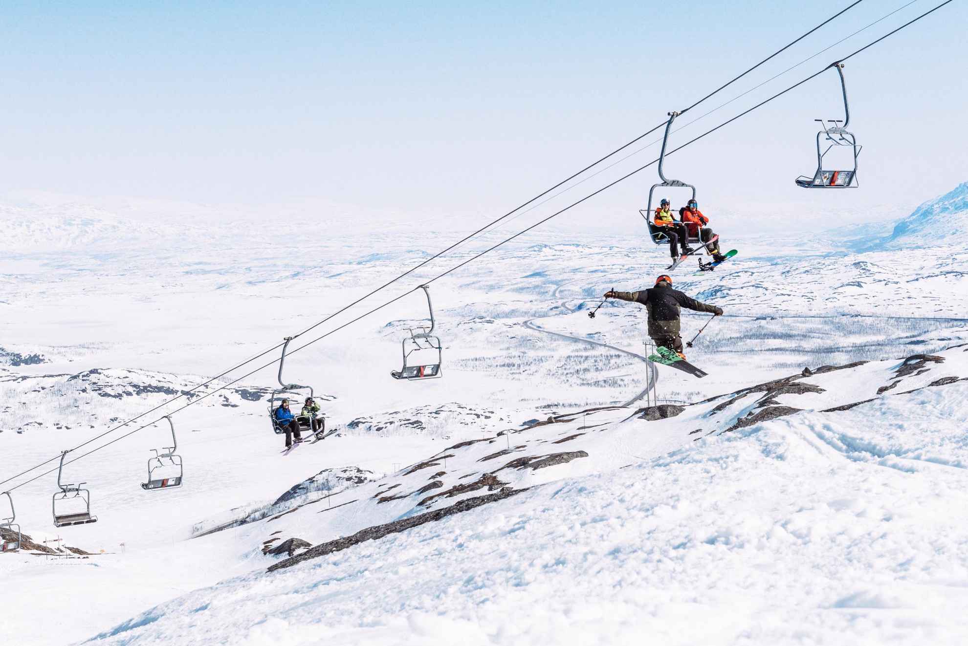 Mensen die op een skilift zitten en kijken naar een persoon die met ski's springt.