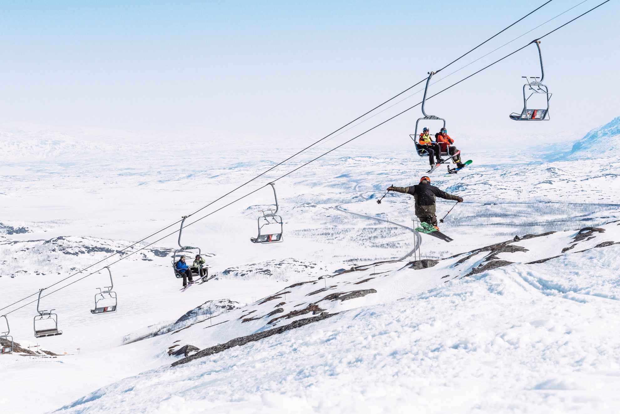Mensen die op een skilift zitten en naar een persoon kijken die met ski's springt.