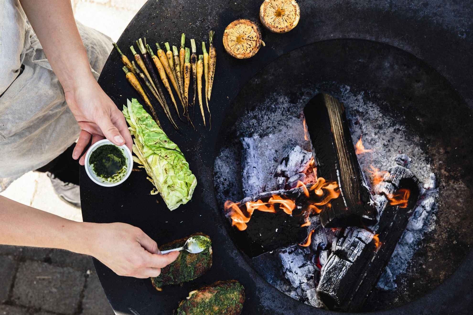 Een chef-kok bereidt eten bij een vuur. Champignons, wortelen, salade en brood staan bij het vuur.