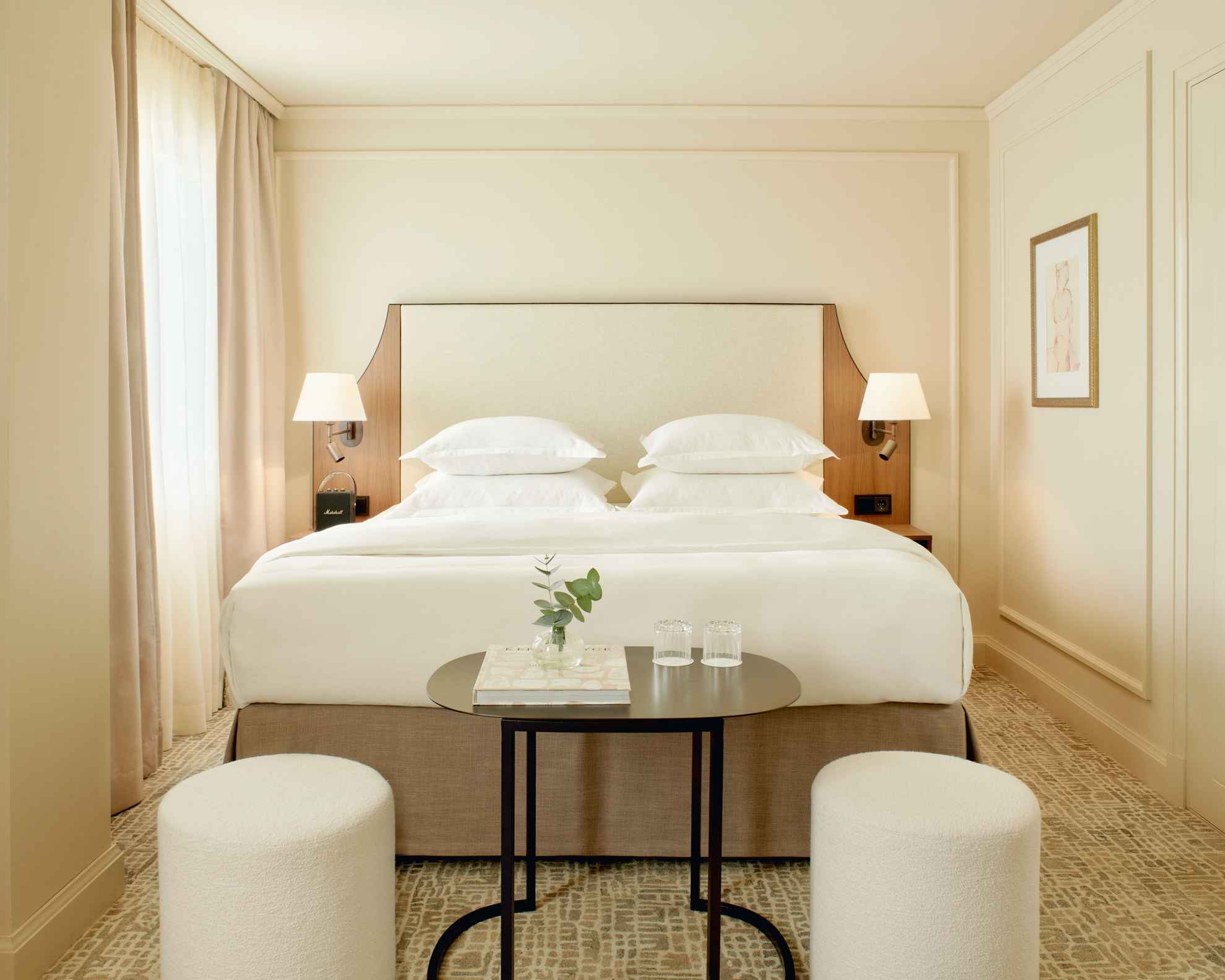 Hotelkamer in Villa Dahlia. De kamer heeft lichtgekleurde muren, een tweepersoonsbed, een donker tafeltje en twee witte zitkussens.