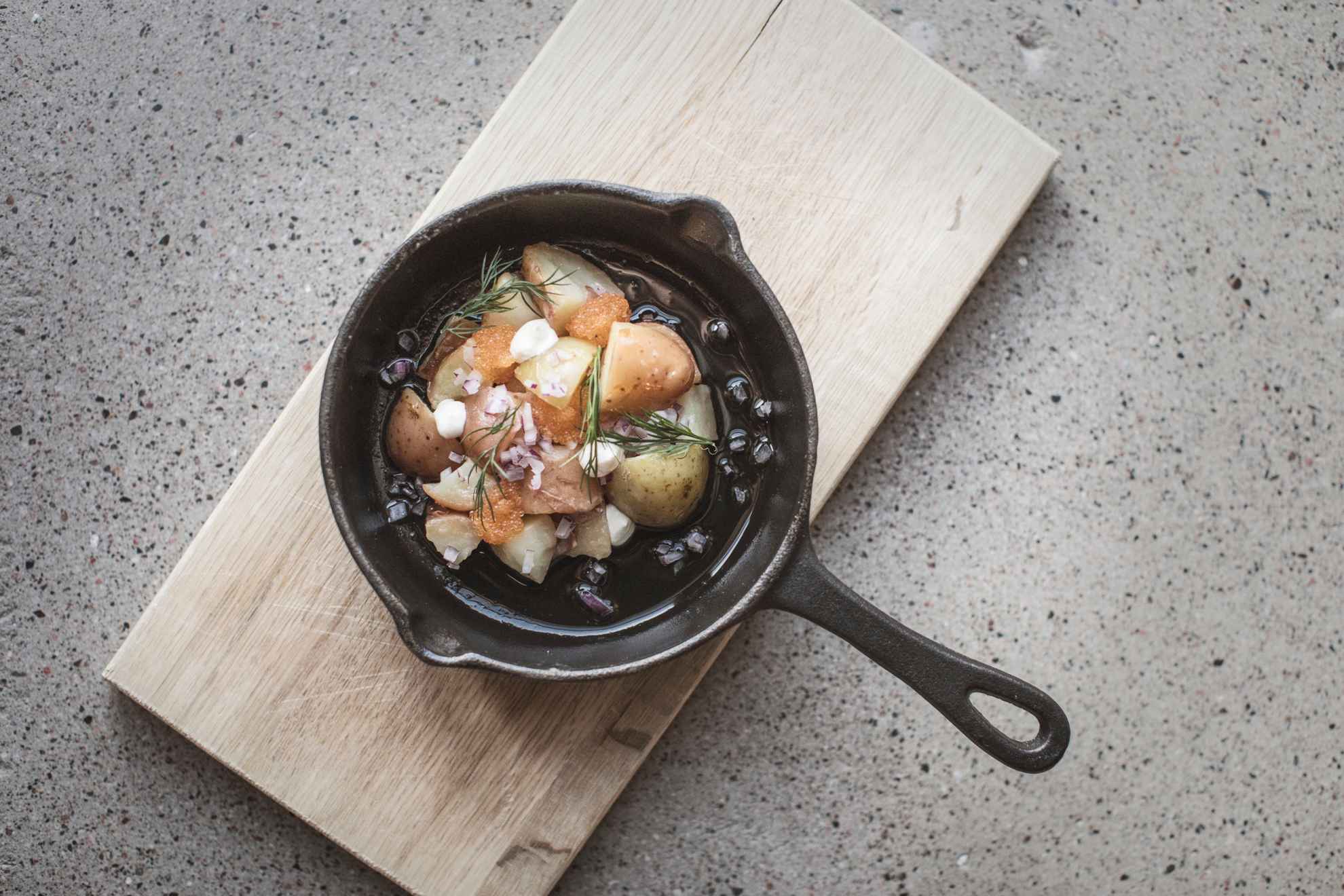Close-up van een gerecht met kaviaar geserveerd met aardappelen en rode ui geserveerd in een ijzeren pan.