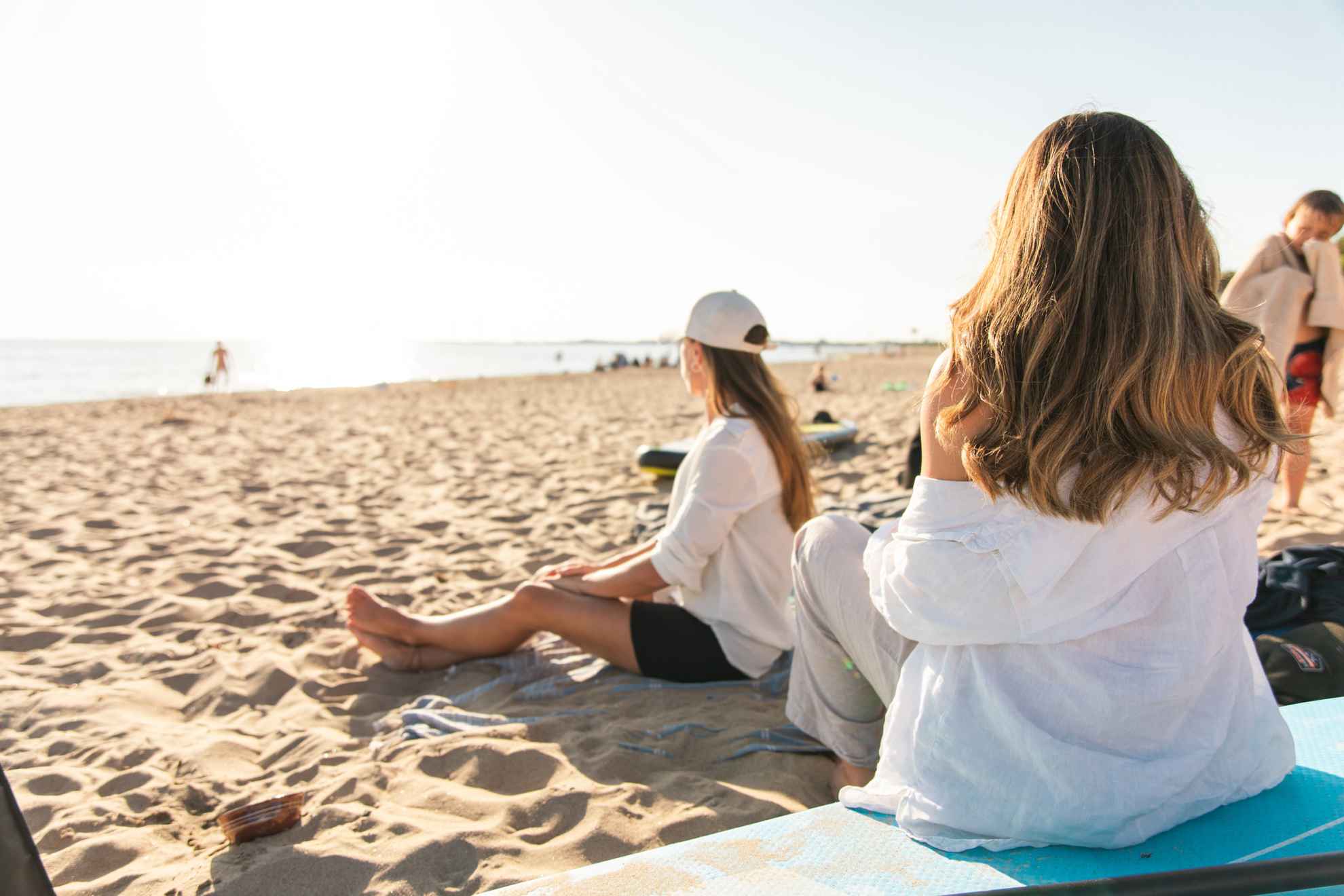 Twee vrouwen zitten op een zandstrand en kijken uit over de oceaan terwijl de zon ondergaat.