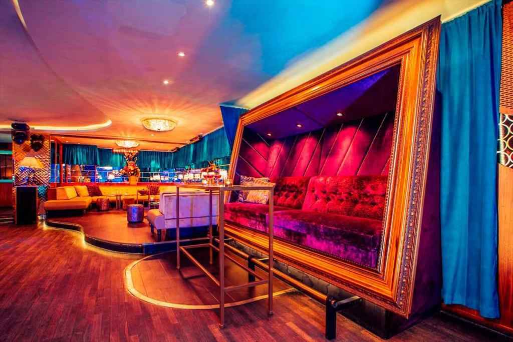 Een nachtclub met fluwelen meubels, houten vloeren en blauwe gordijnen.