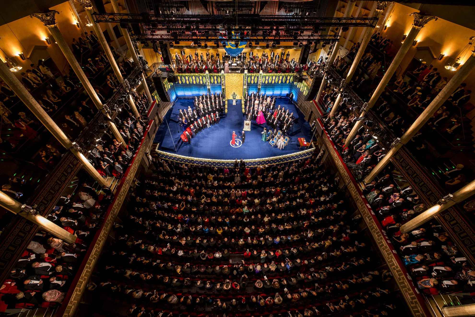 Een zaal vol mensen kijkend naar het podium waar laureaten hun Nobelprijs ontvangen.