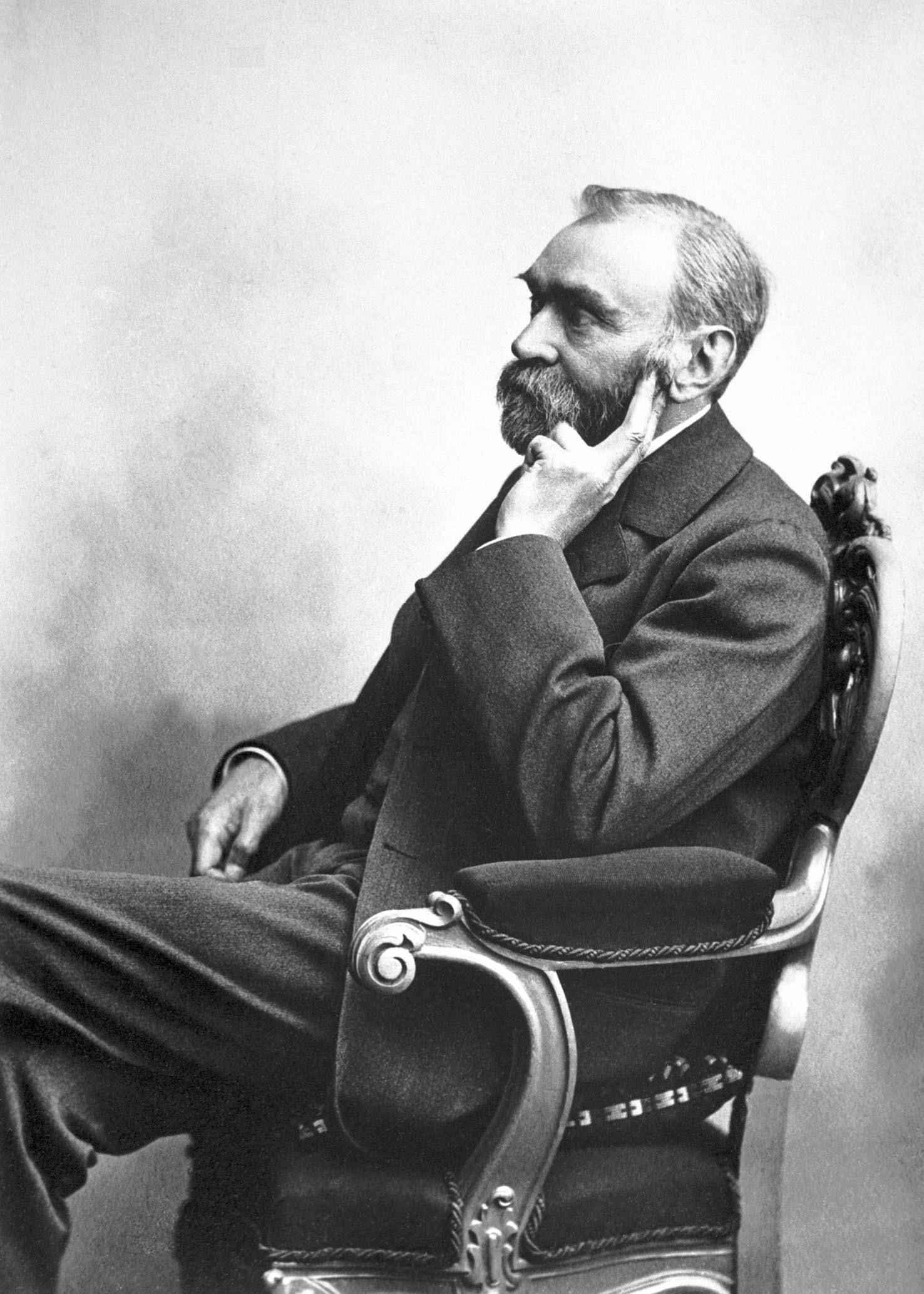 Een zwart-wit oud portret van Alfred Nobel zittend in een stoel.