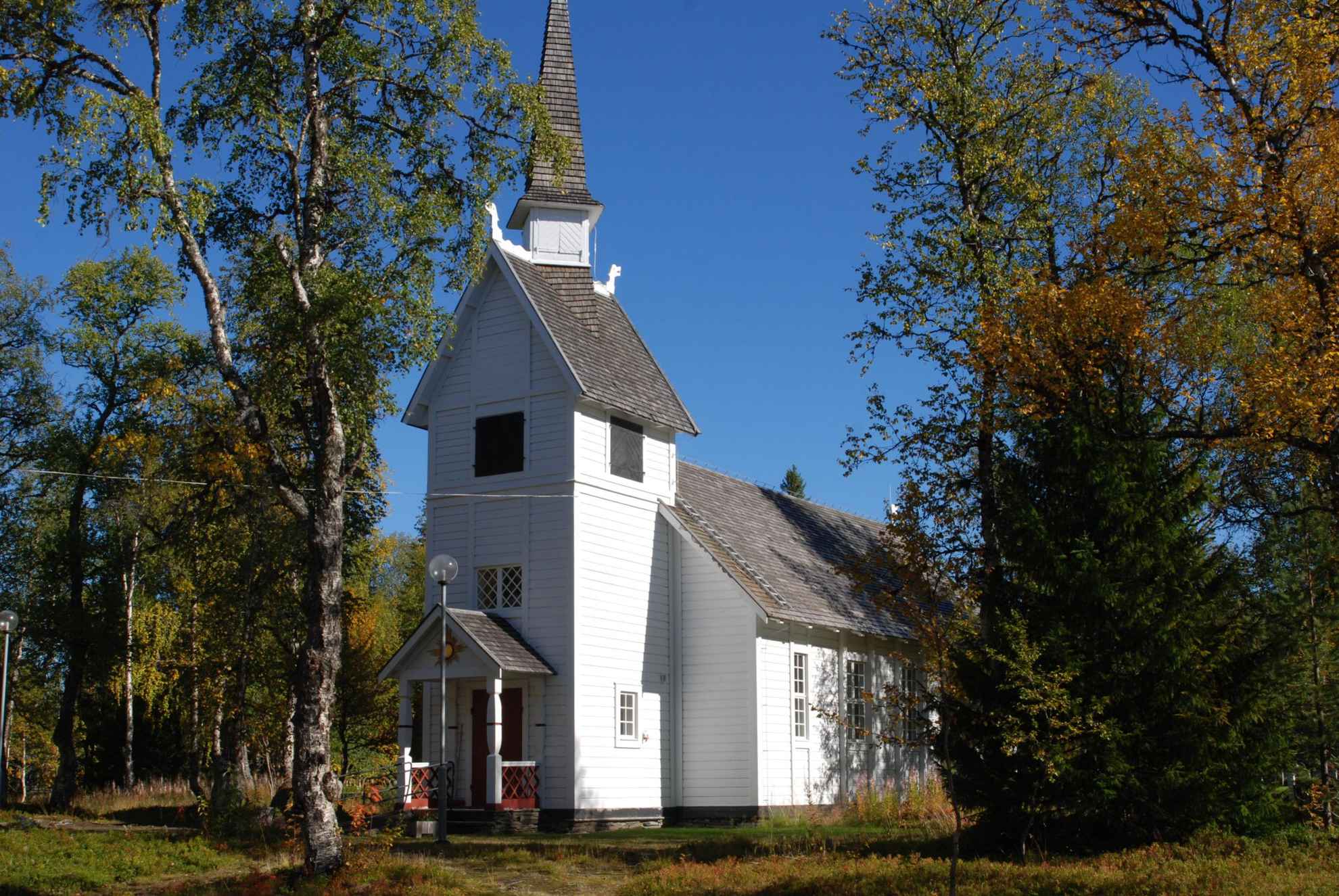 Een witte kapel omgeven door herfstkleurige loofbomen.