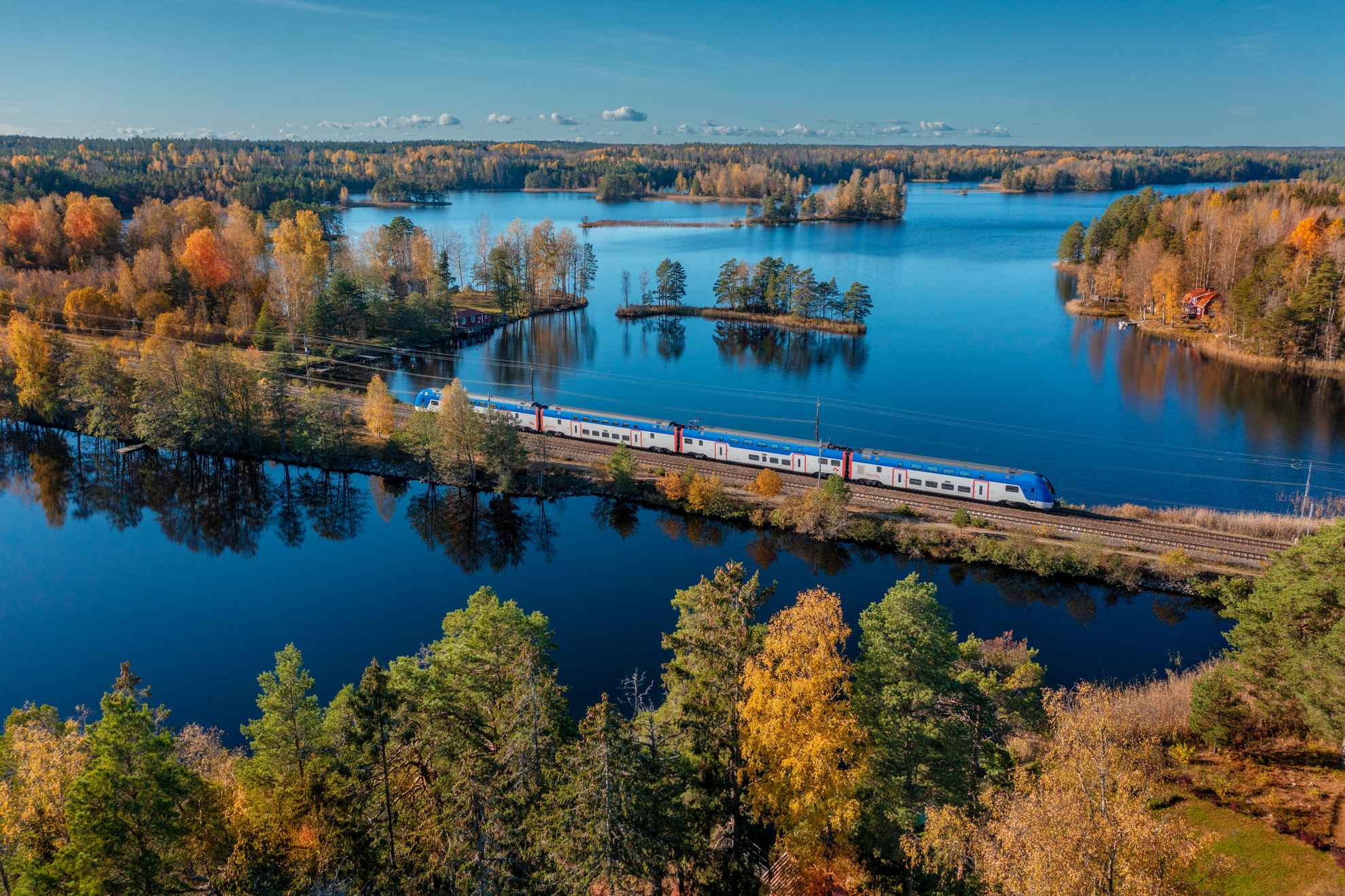 Een luchtfoto van een trein die door een boslandschap met meren in de herfst rijdt.