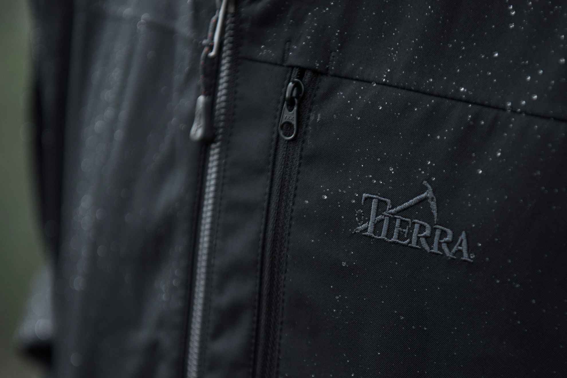 Een close-up van een zwarte jas met het geborduurde logo van het merk Tierra.