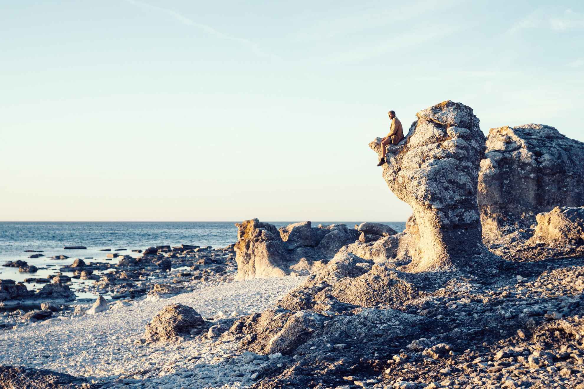 Zeerotsen met de zee op de achtergrond. Een persoon zit op een rots.