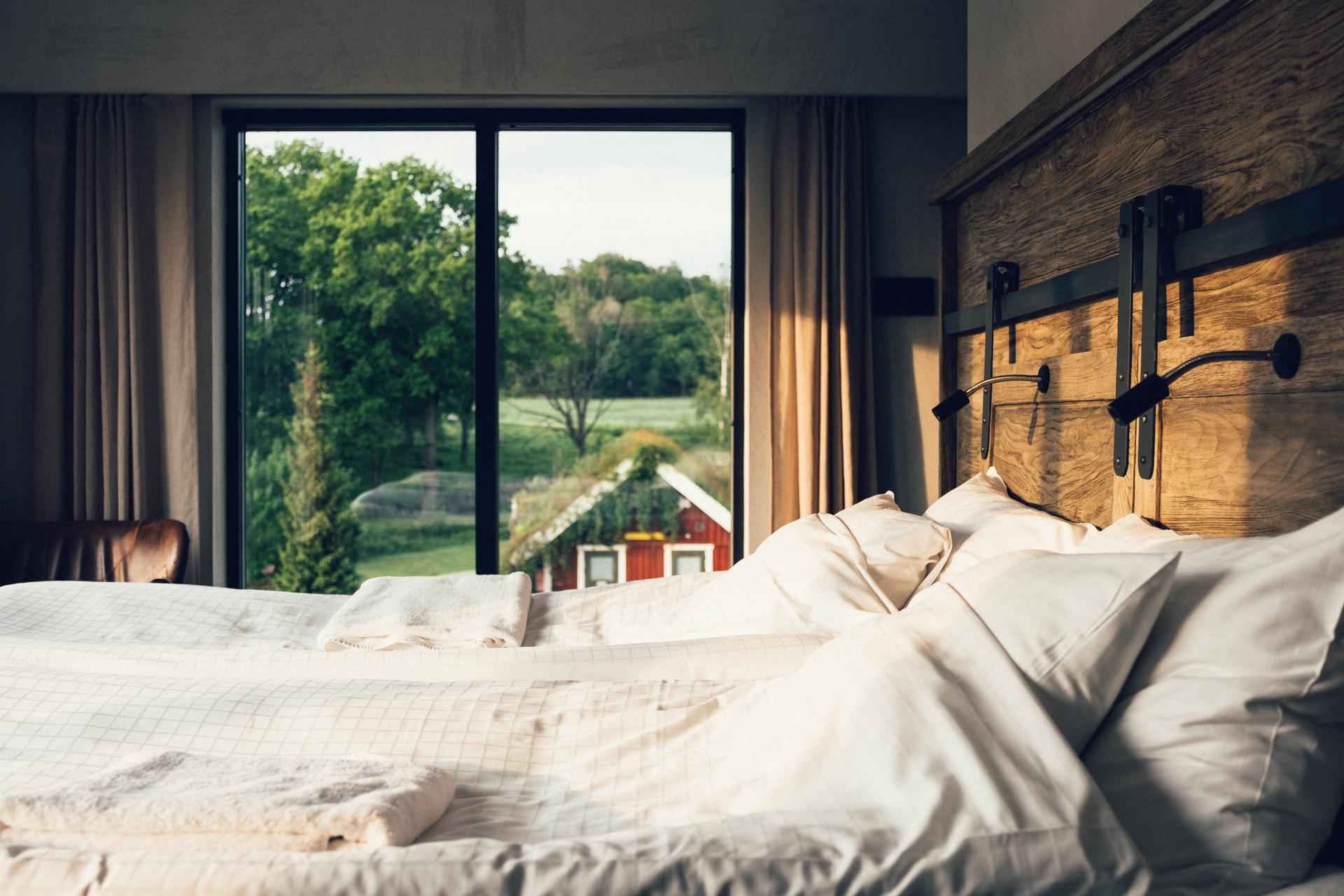 Een tweepersoonsbed in een hotelkamer met ramen die uitkijken op een rode hut en een bos.