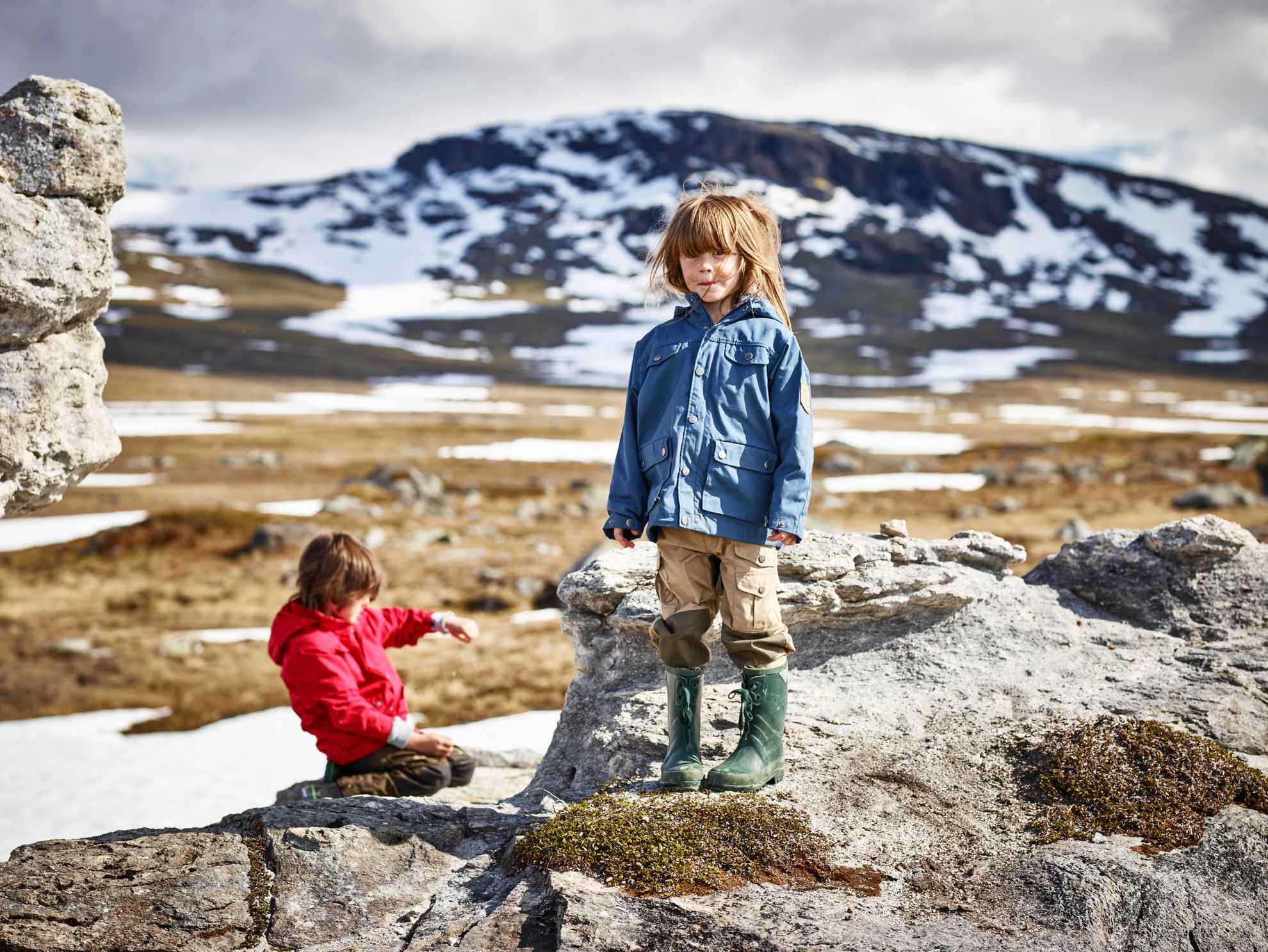 Twee kinderen op een wandeling in Padjelanta in Noord-Zweden, omringd door sneeuwvlaktes en bergtoppen.