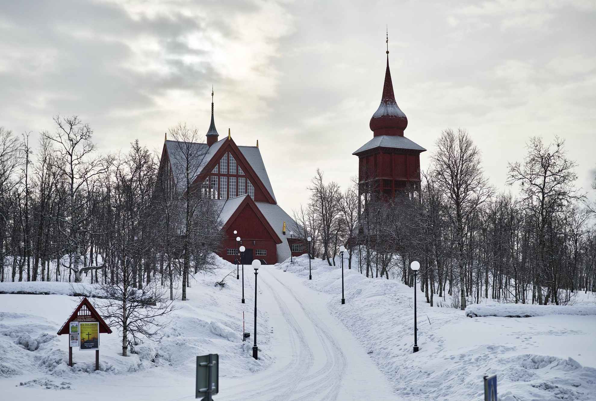 De Kiruna-kerk, een houten gebouw met een aparte klokkentoren, ligt op een met sneeuw bedekte helling.