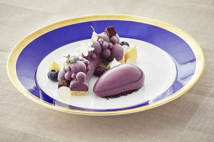 Een paars dessert met garnituur op een bord in wit en blauw met een gouden randje.