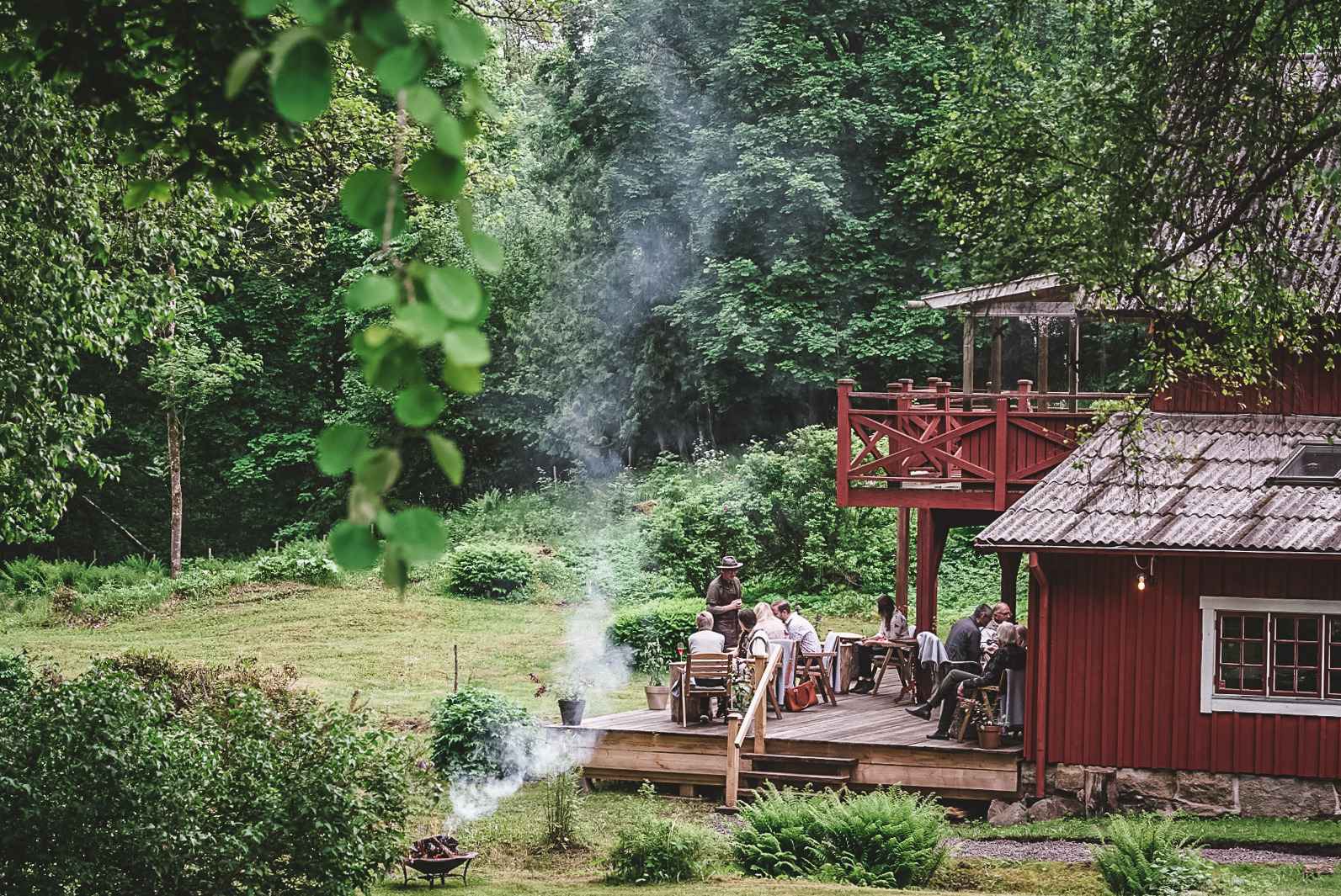 Een rood houten huis in de zomer. Mensen zitten op de patio.