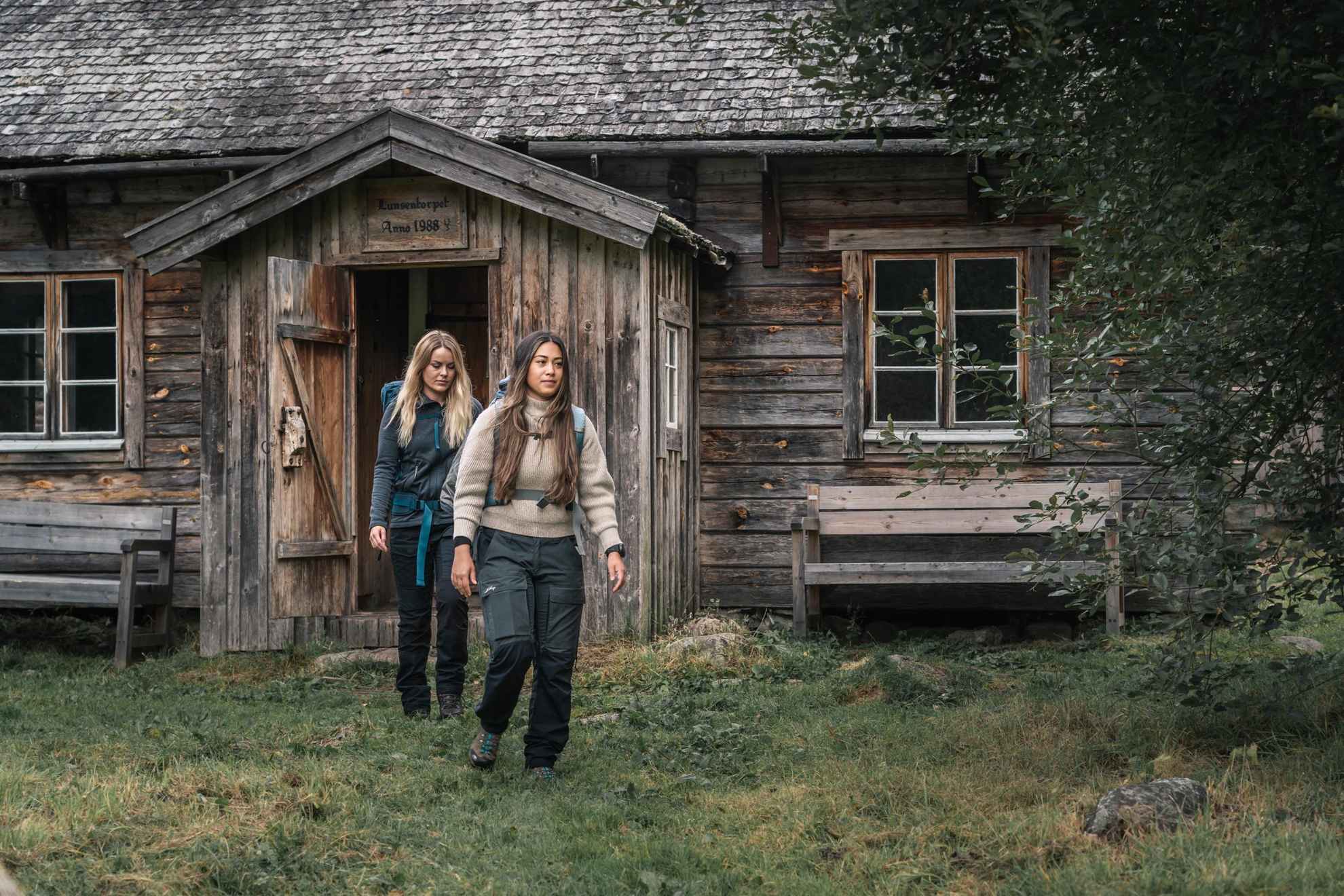 Twee vrouwen verlaten een houten huisje in het bos.