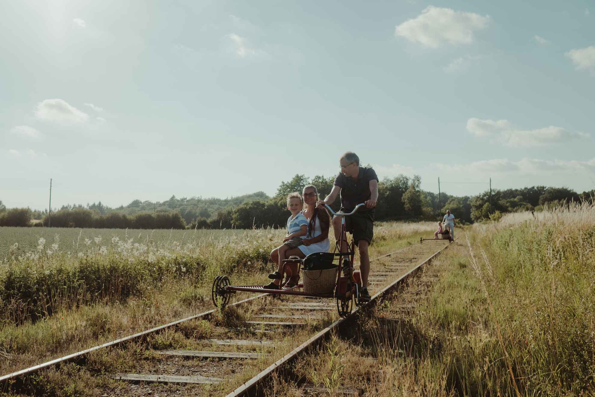 Een gezin op een trolleyfiets op een oude spoorlijn, omgeven door velden.