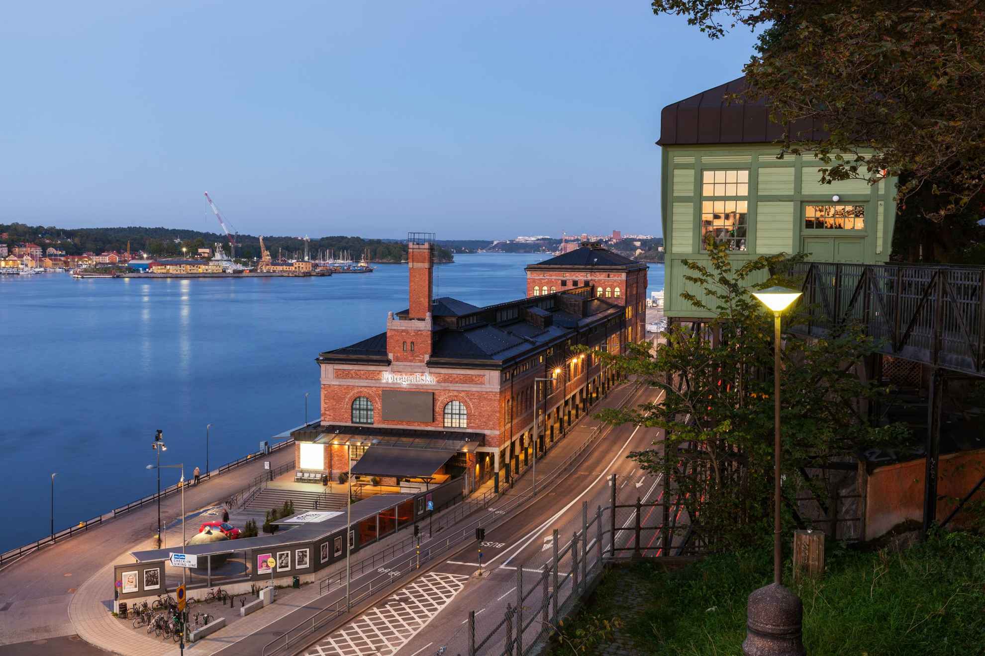 Het museum Fotografiska, gezien vanaf de heuvel erboven. De zee en delen van Stockholm op de achtergrond.