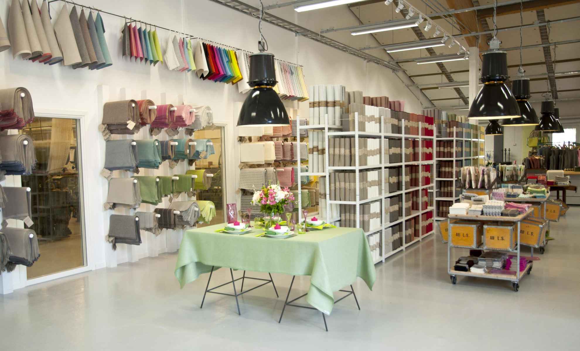 Interieur uit een fabriekswinkel met linnen producten. Planken en tafels met linnen textiel en producten. Een tafelset met een groen tafelkleed en servetten.