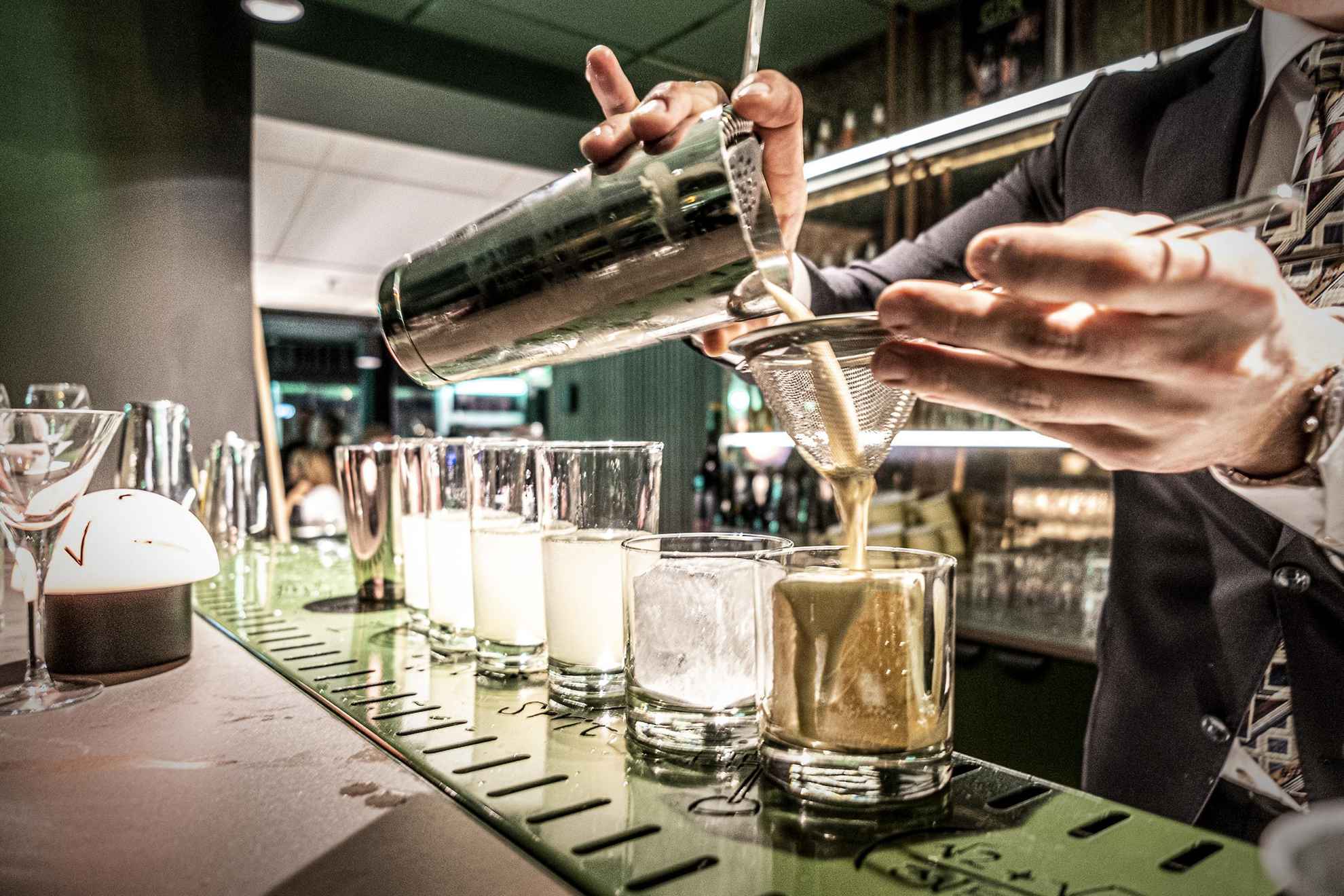 Een barman die een cocktail uit de shaker in een glas giet.