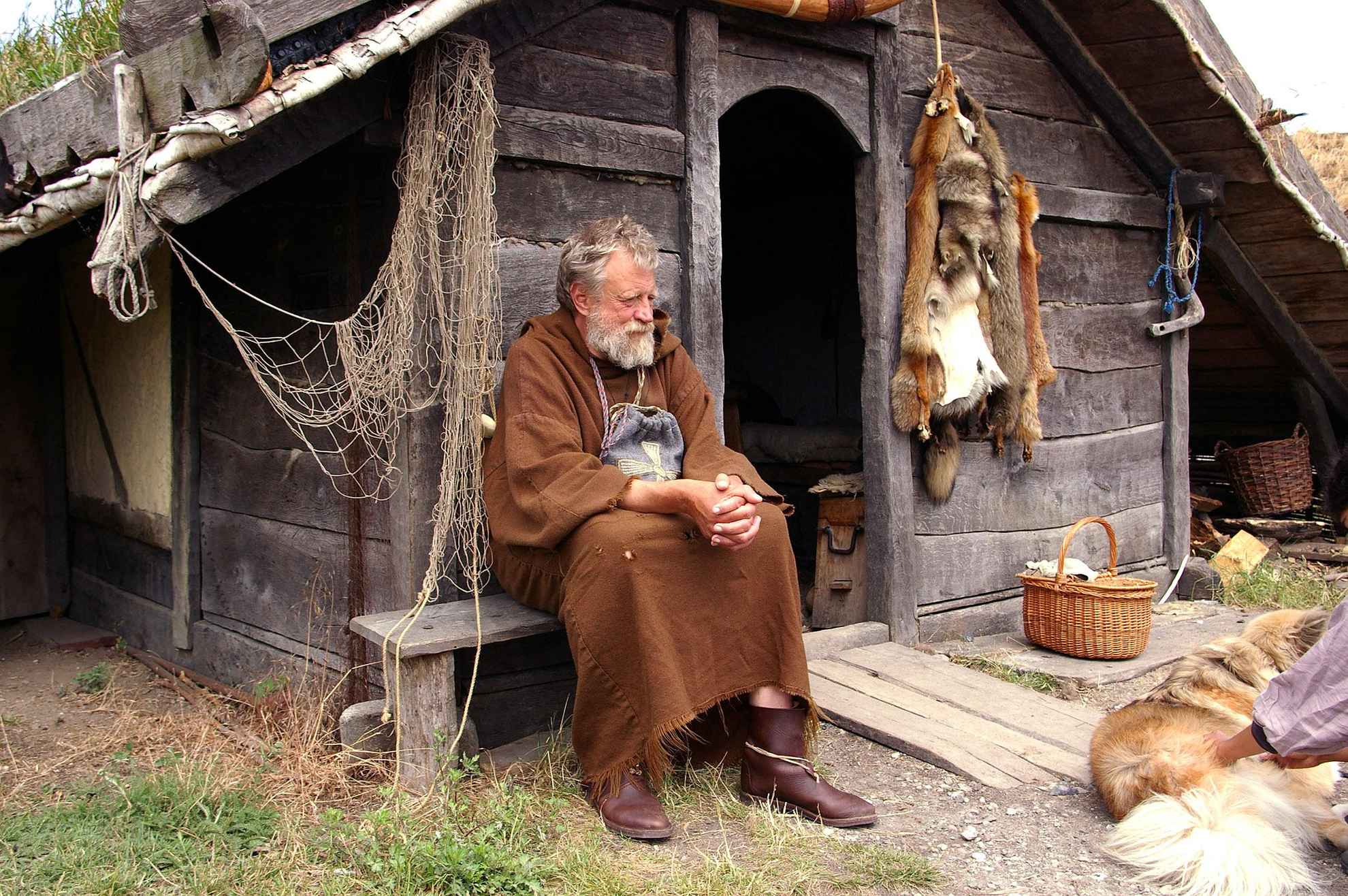 Een oude man verkleed als Viking zit voor een oud houten huis.