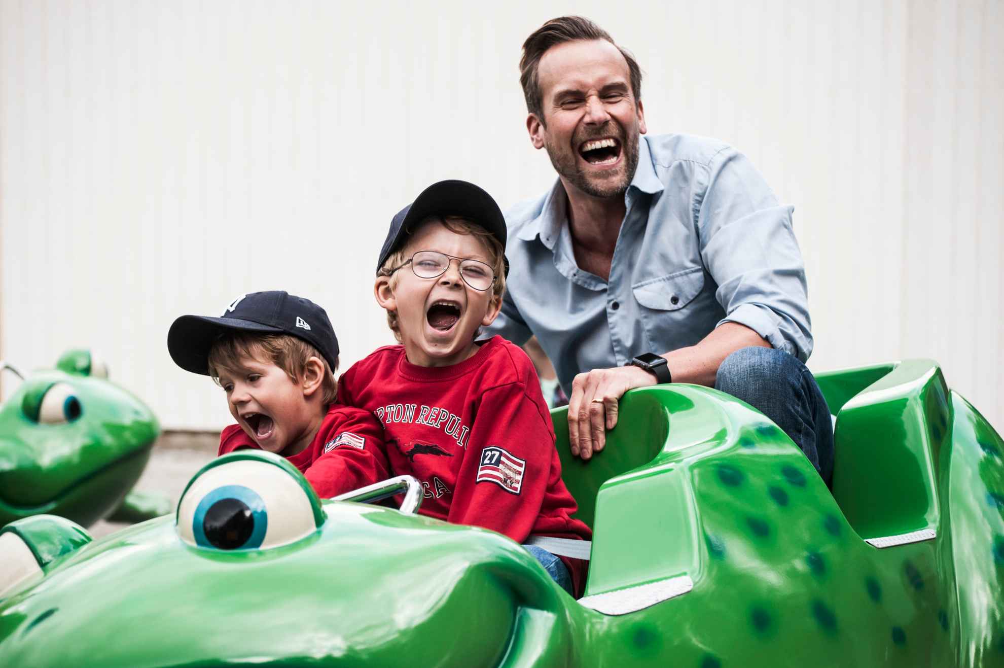 Twee lachende jongens in gezelschap van een man in een groene achtbaan bij Furuvik.