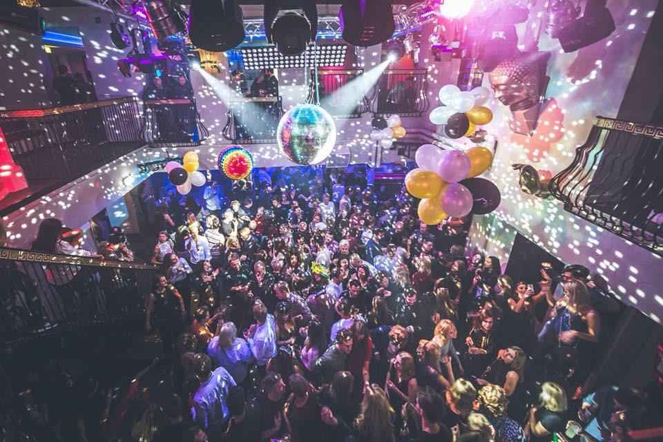 Mensen dansen in een nachtclub. Aan het plafond hangen ballonnen en decoratie.