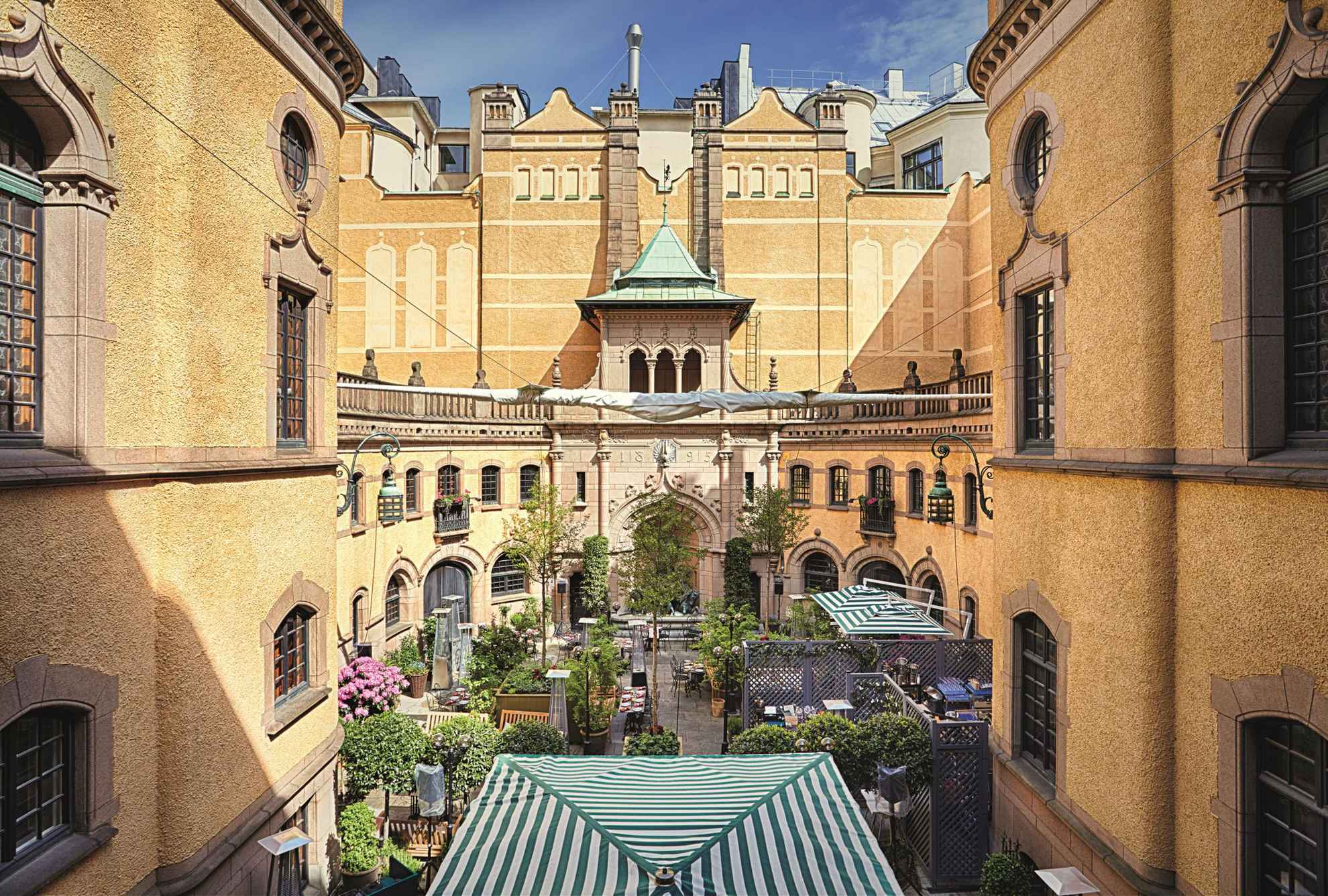 Het gebouw van het Hallwyl Museum in Stockholm. De binnenplaats met veel planten, tafels en een paar groen-wit gestreepte parasols.