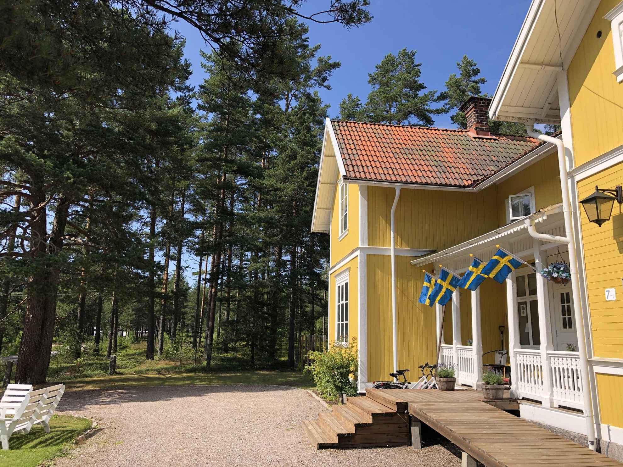 Een geel houten huis met vier Zweedse vlaggen, de buitenkant van Hedenstugan B&B Hotell.