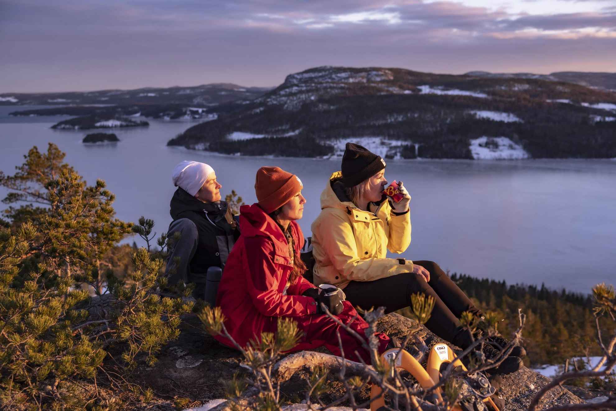 Drie mensen genieten in de winter van de zon met een kopje koffie bovenop een heuvel.