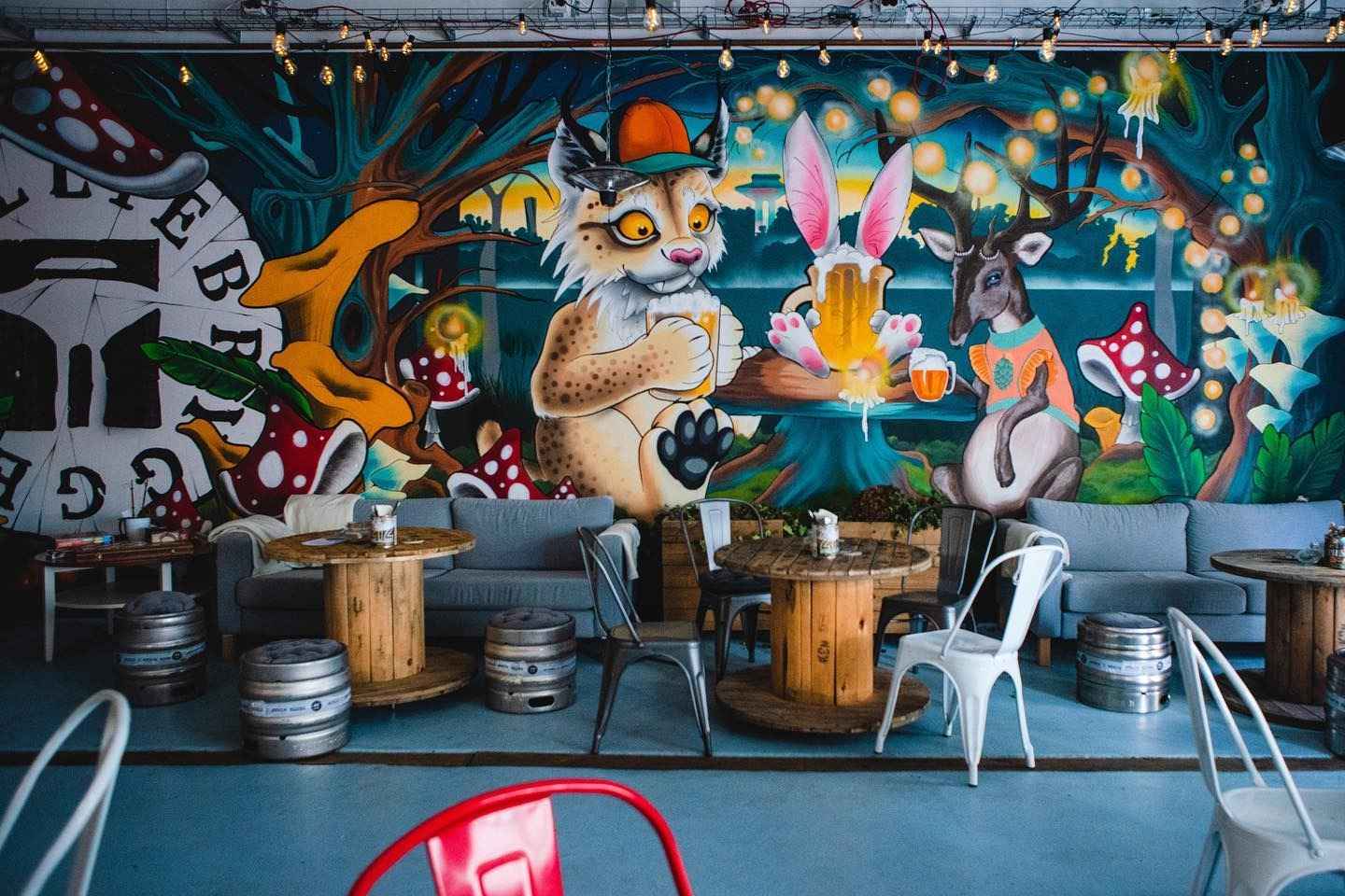 Houten tafel met biervaten als stoelen, met daarachter een kleurrijke grafietwand.