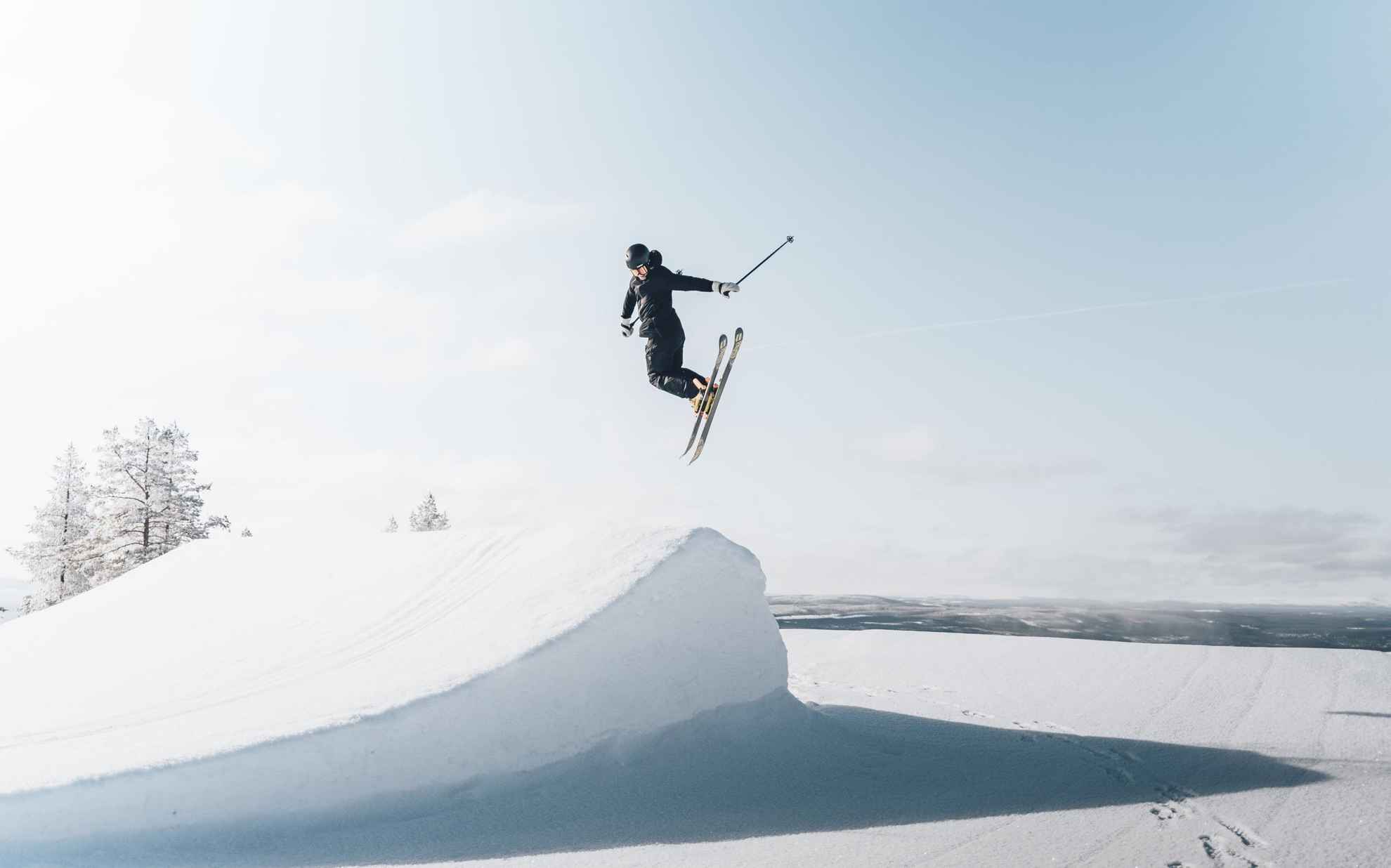 Een skiër doet een jump in een wit landschap.