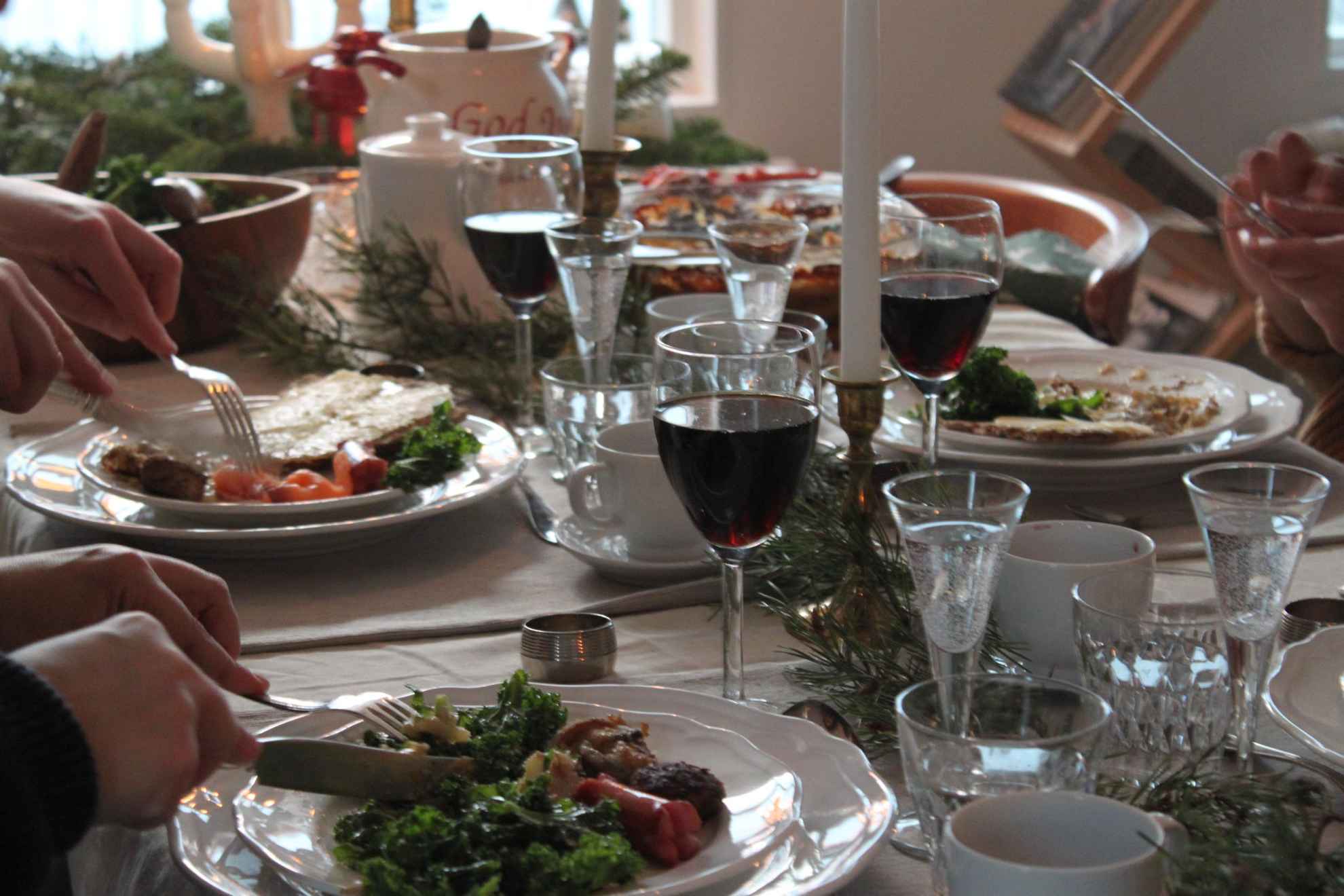 Close-up van een gedekte tafel waar je de handen ziet van mensen die een kerstlunch eten.