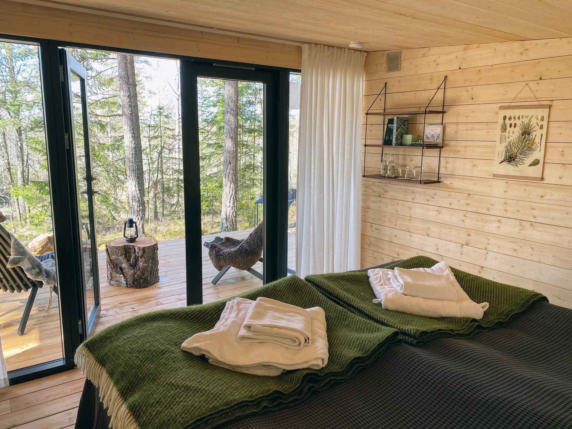 Twee bedden staan in een kamer met houten wanden en vloer. De kamer heeft glazen deuren naar een patio met twee stoelen met uitzicht op de natuur.