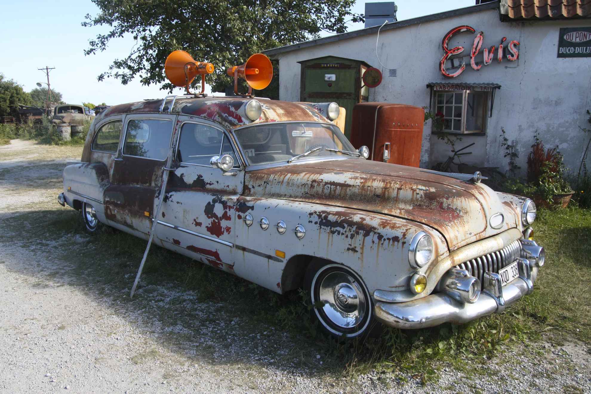 Een oude roestige auto met sirenes op het dak voor een oud benzinestation.