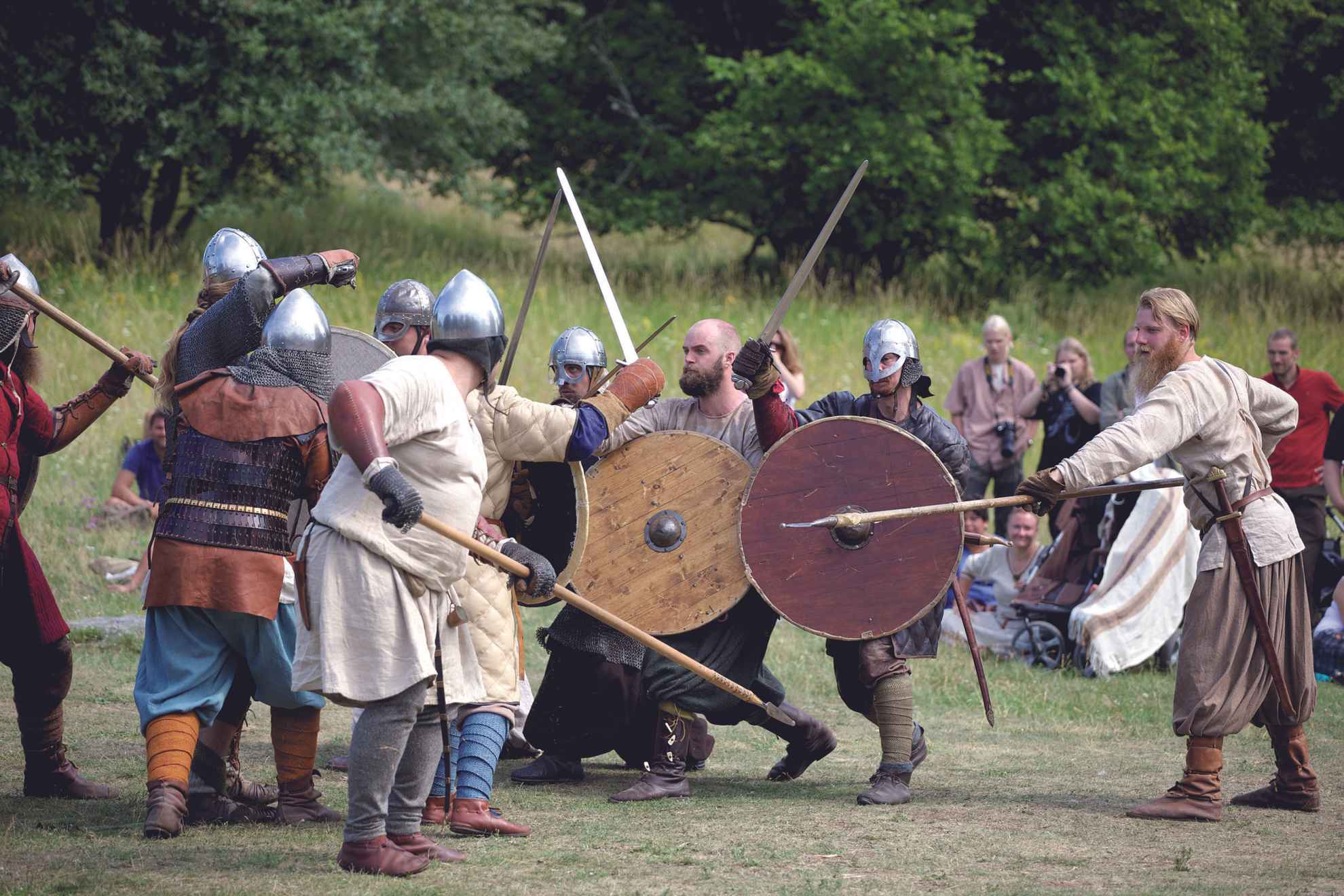 Een groep mensen, allemaal gekleed in vikingkleding, speelt een gevecht na met speren, zwaarden en schilden.