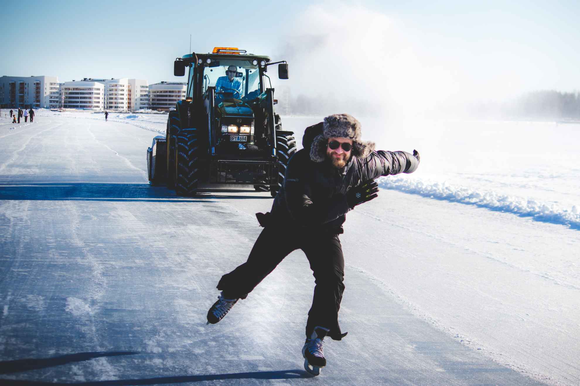 Een man gekleed in het zwart schaatst op het ijs met een tractor achter hem.