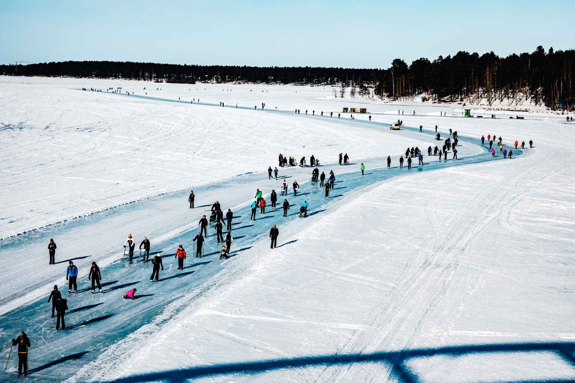Mensen lopen en schaatsen op de zonnige ijsbaan rond Luleå.