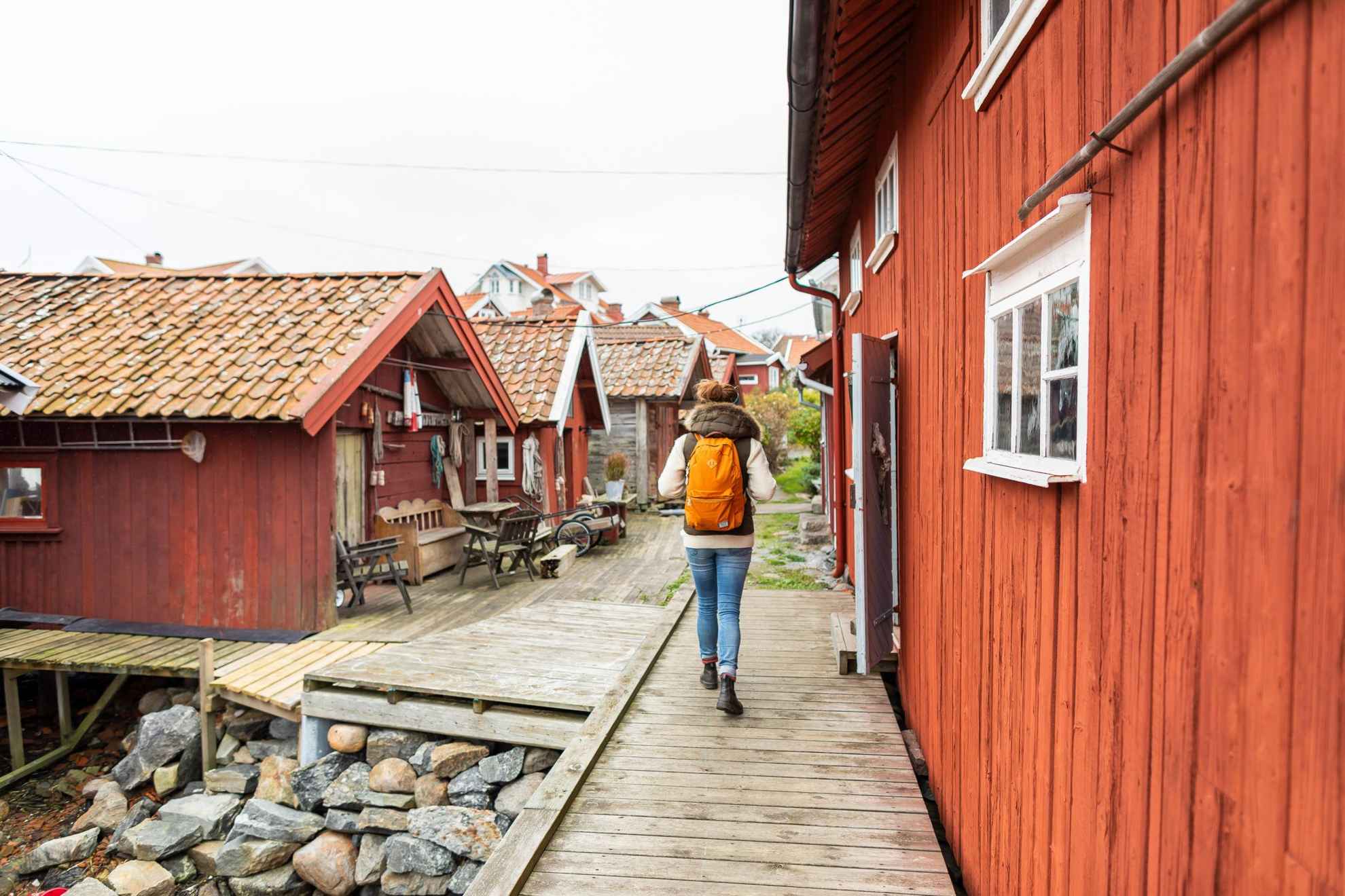 Een persoon met een rugzak loopt tussen rode houten huizen.