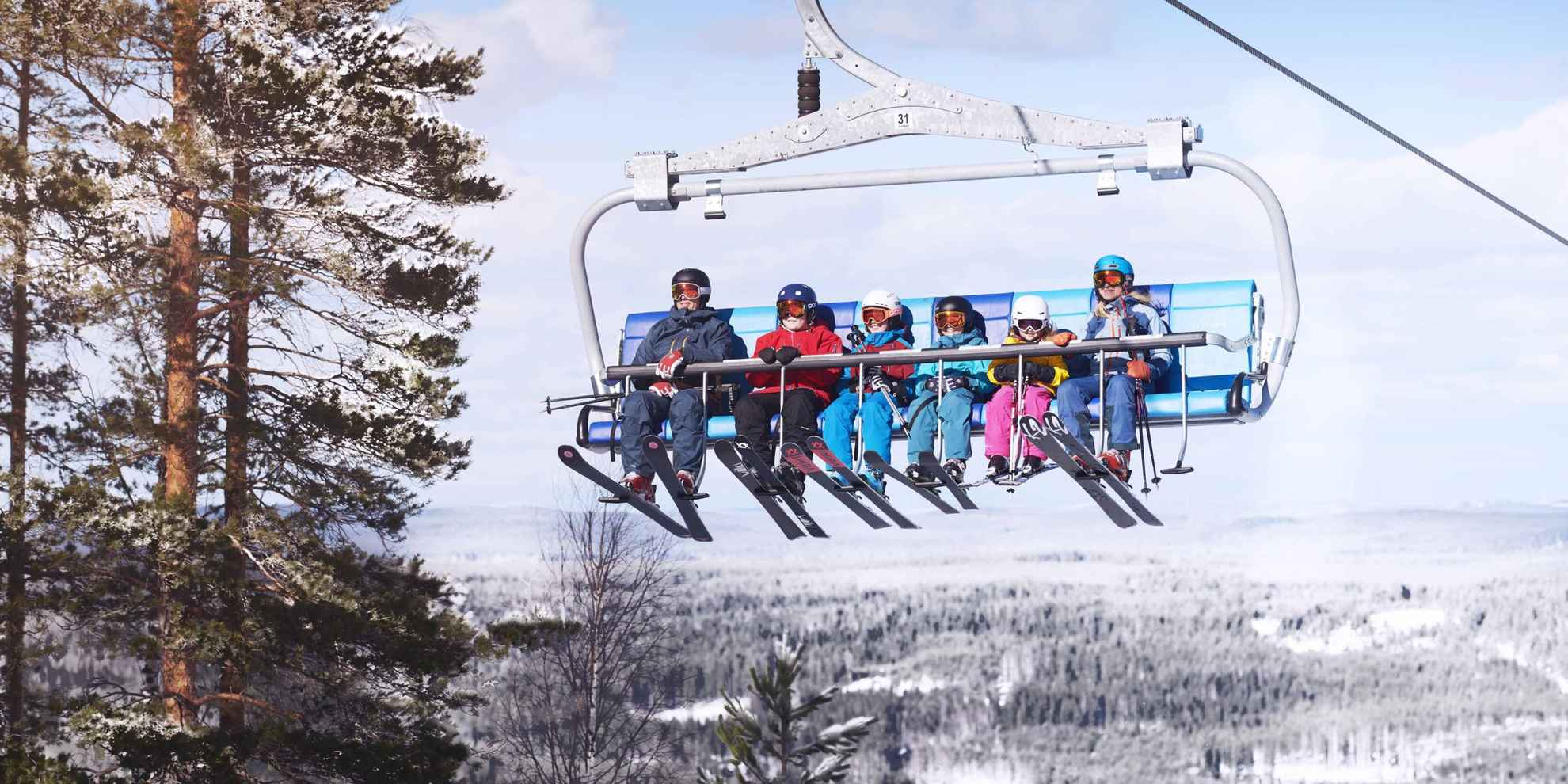 Een gezin van zes personen zit in een skilift met skiuitrusting die in de winter een heuvel op gaat.