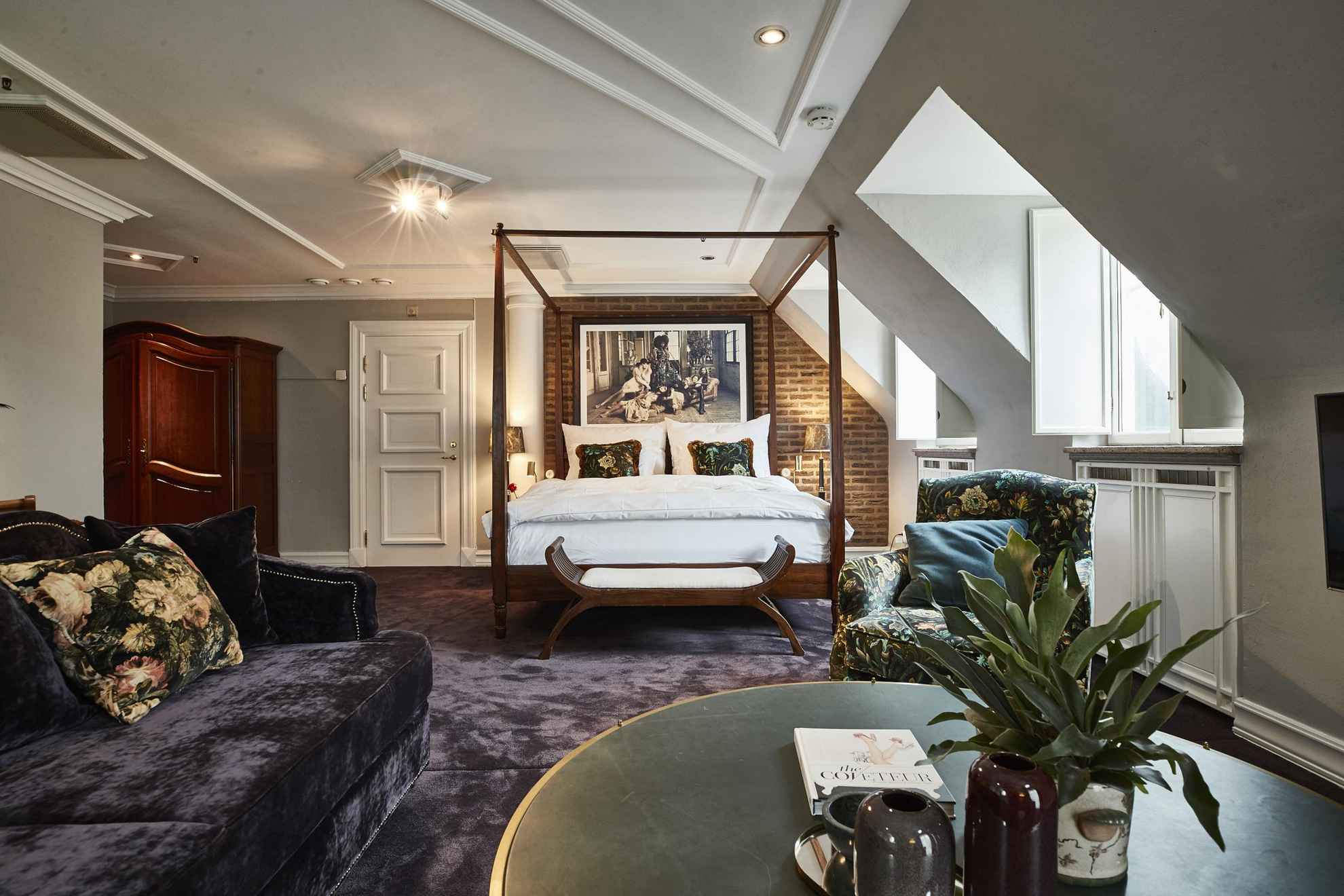 Een grote hotelkamer met fluwelen tapijt en bank, een groene salontafel, een tweepersoonsbed en een houten kast.