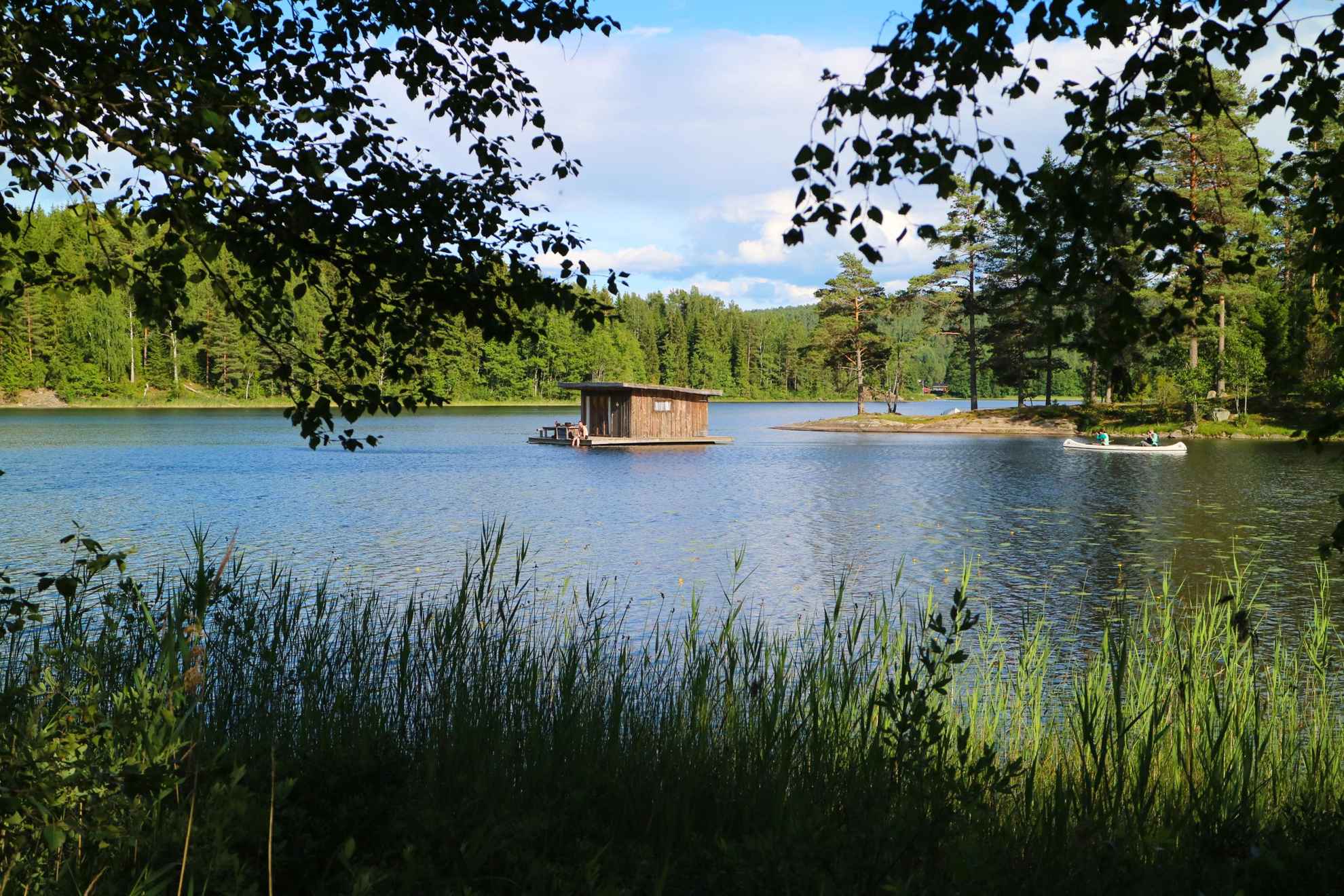 Een huisje drijvend in een meer bij Naturbyn en iemand die er langs komt in een kano. Het meer is omgeven door bos.