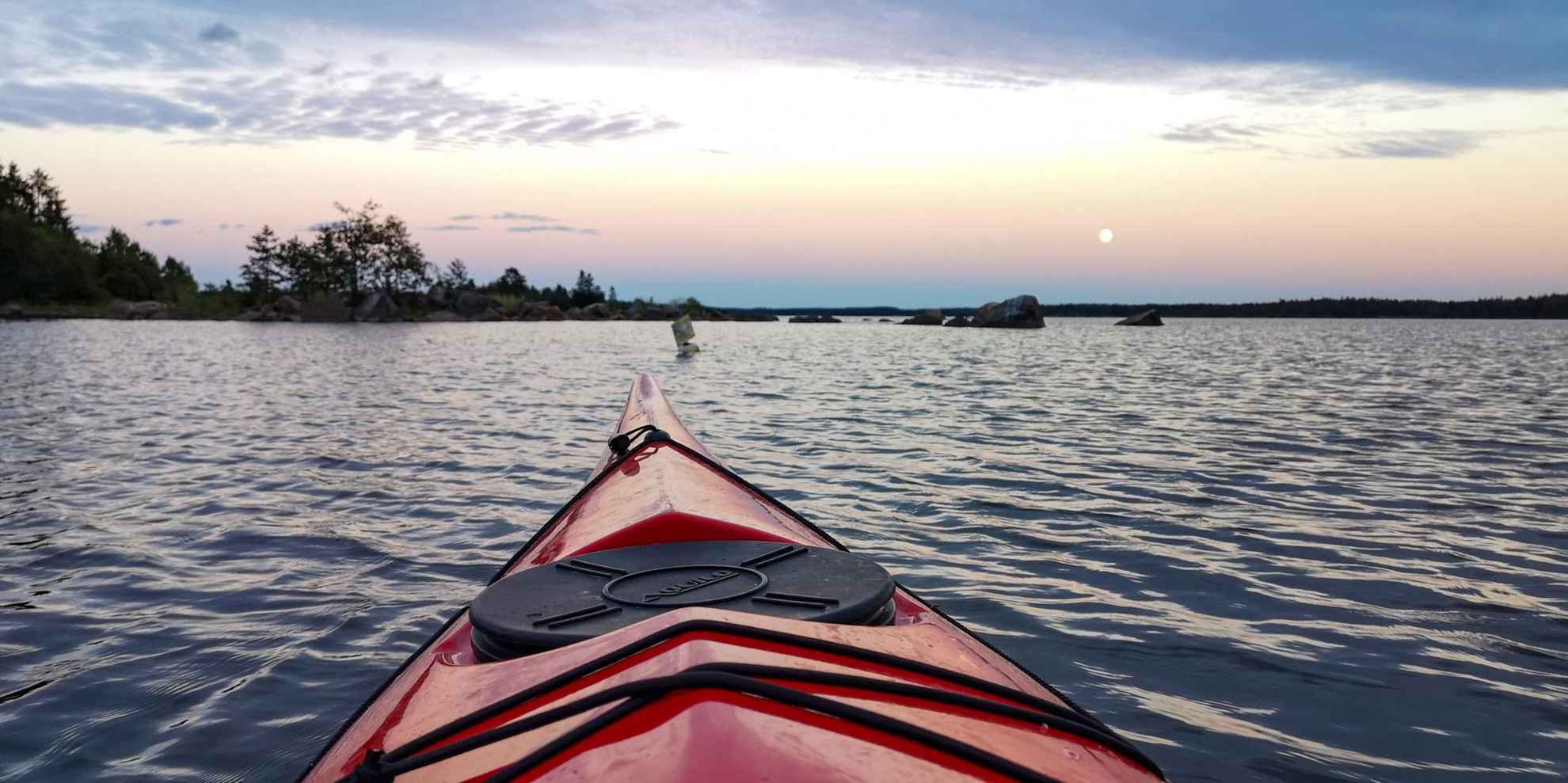 Het voorste deel van een rode kano op het water in de archipel. De zon gaat onder.