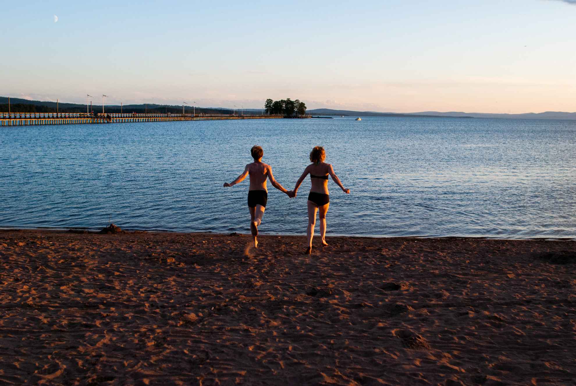 Twee mensen in badpakken rennen over een strand richting het water.
