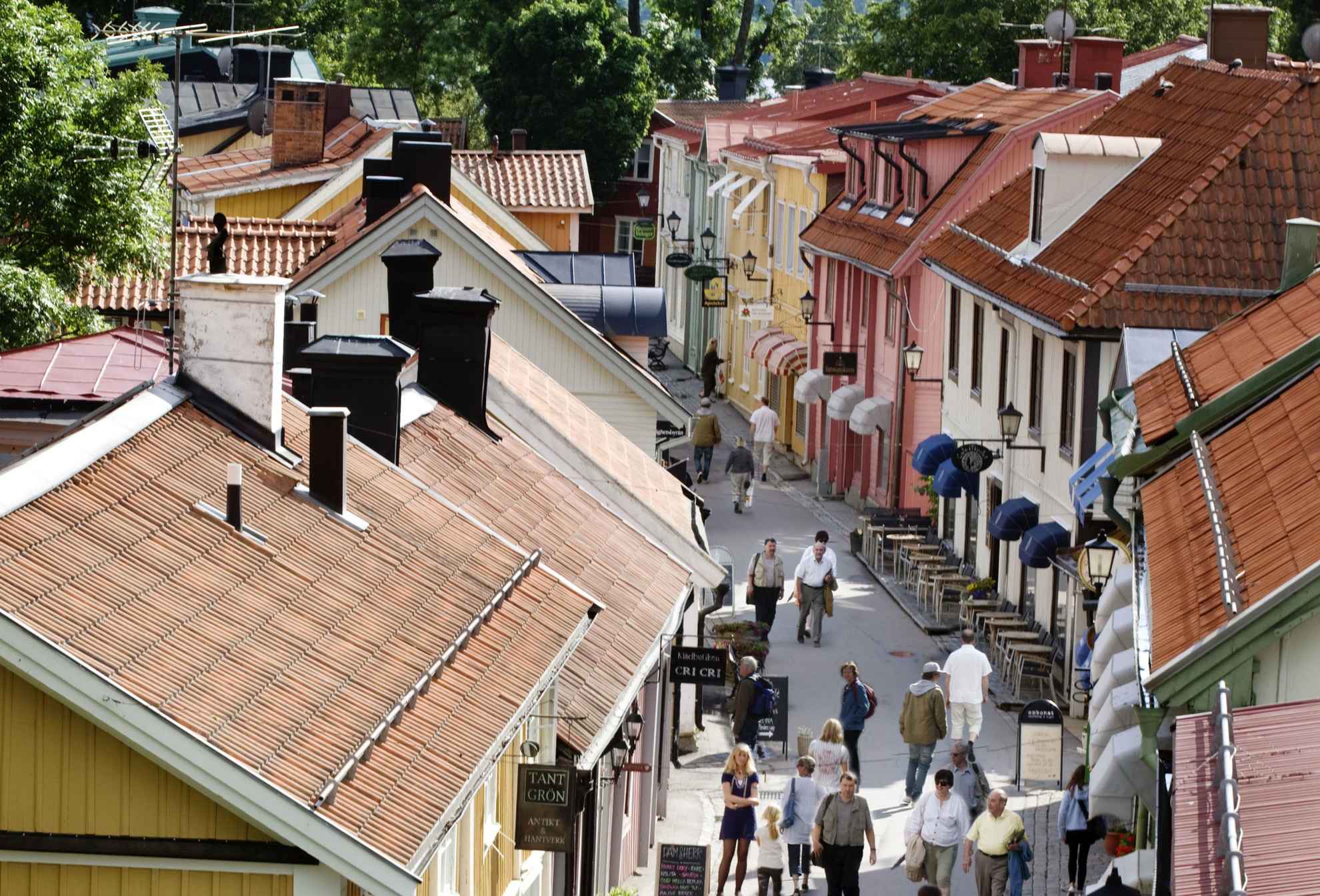 Houten huizen in verschillende kleuren op een smal straatje in Sigtuna, mensen lopen op straat.