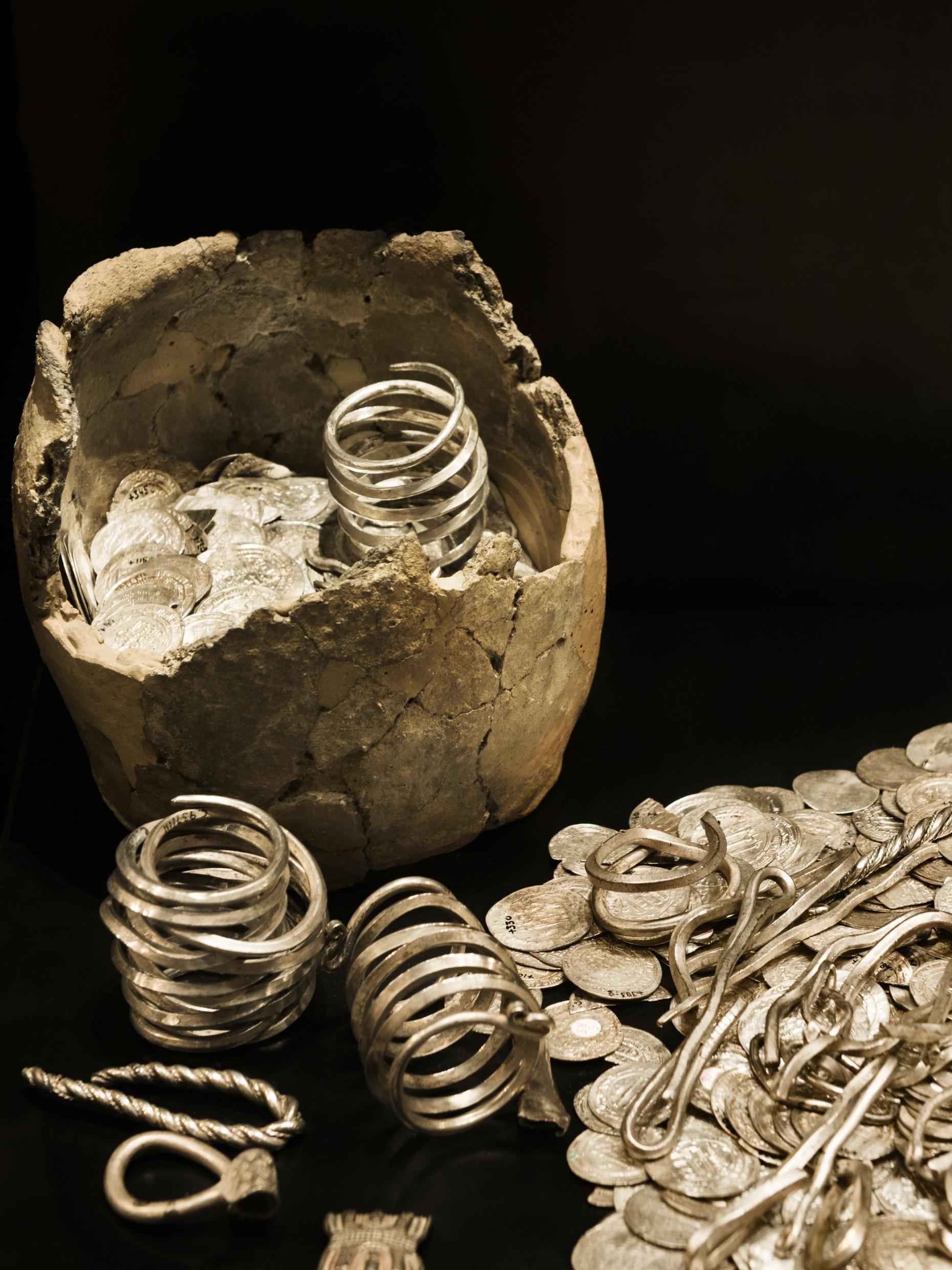 Oude zilveren en gouden munten en sieraden op een zwarte ondergrond.