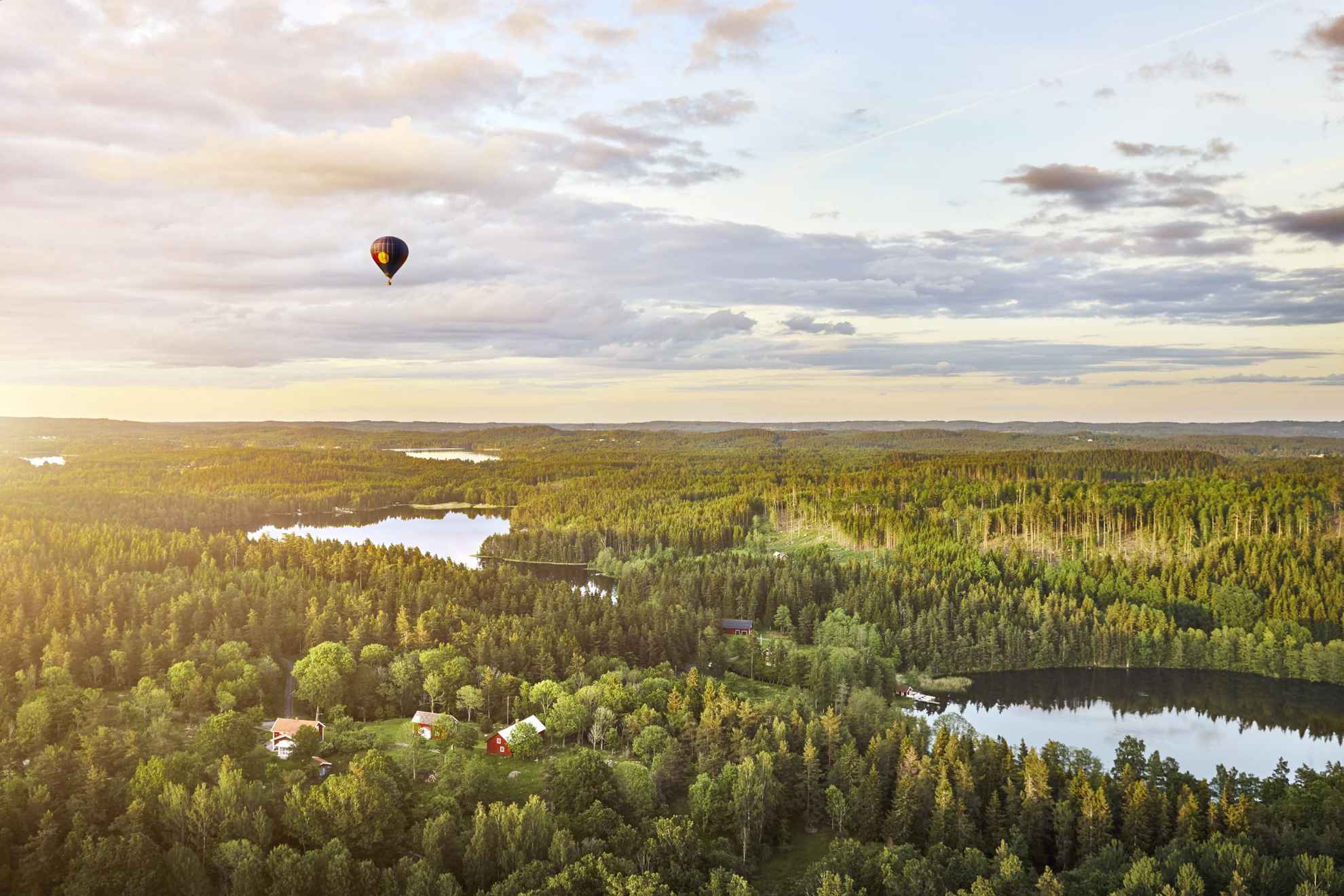 Een heteluchtballon die over bossen, meren en rode huisjes in Zweden vliegt.