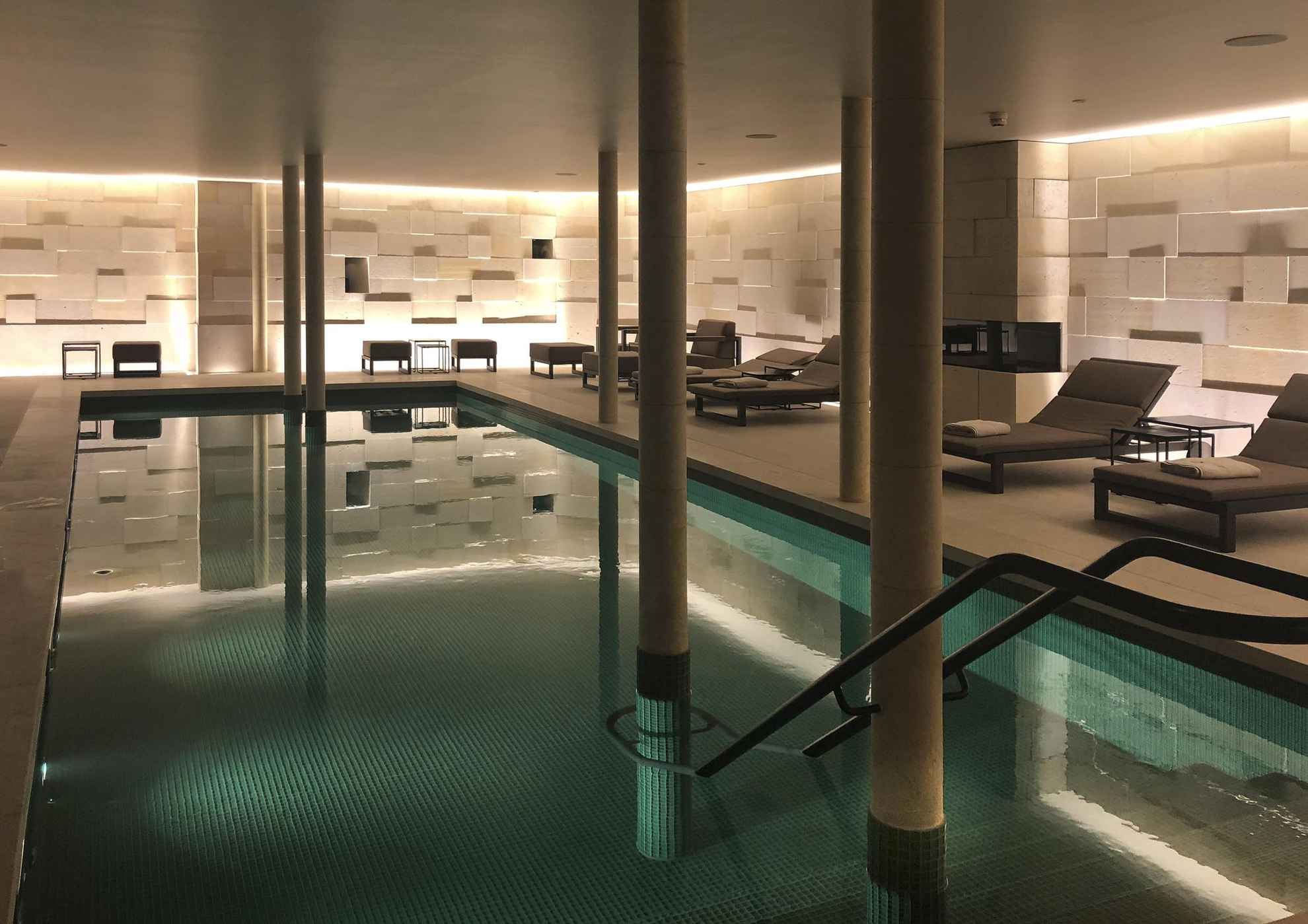 Een schemerige kamer met ligstoelen en een binnenzwembad.