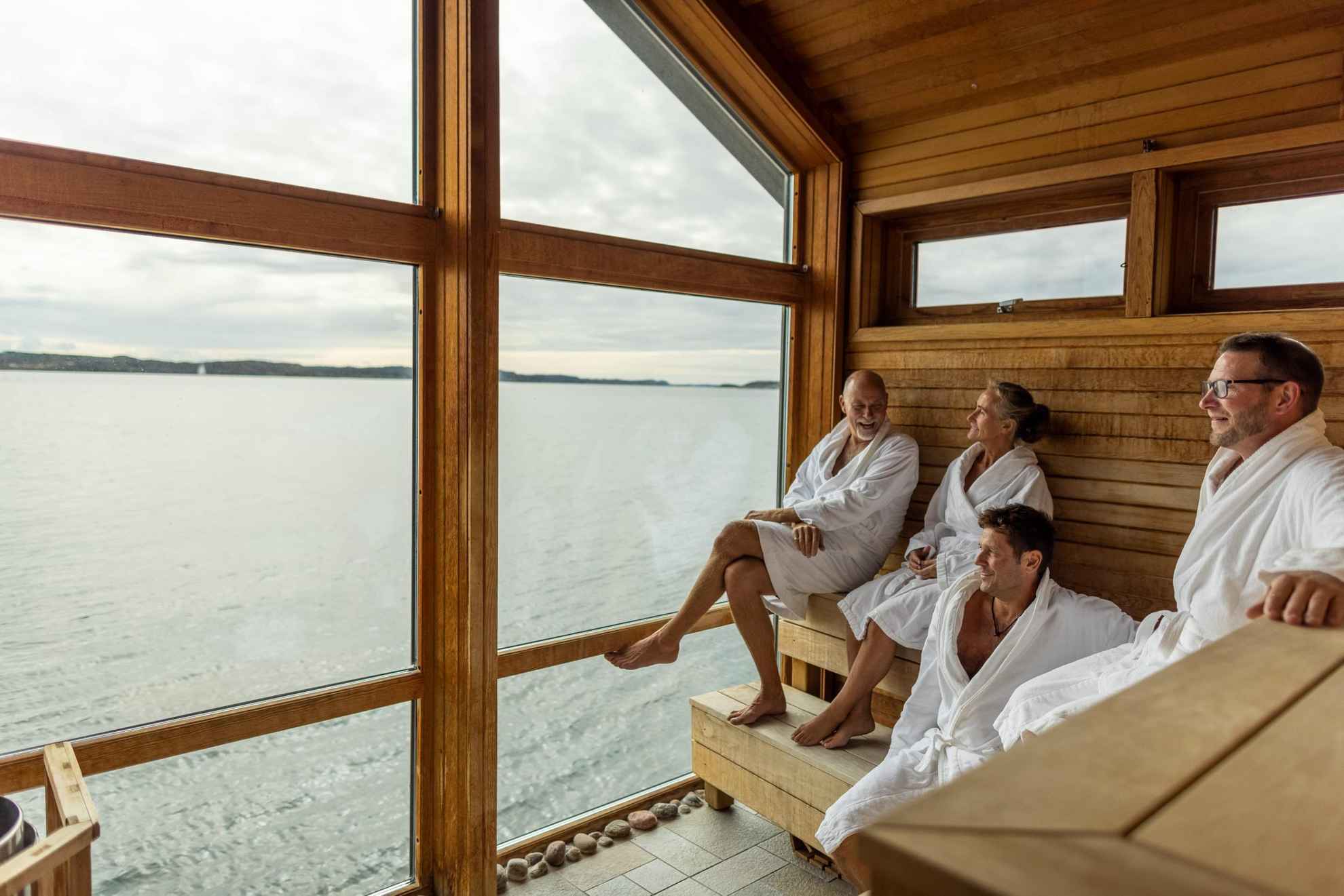 Vier personen genieten van de sauna en het uitzicht op zee.